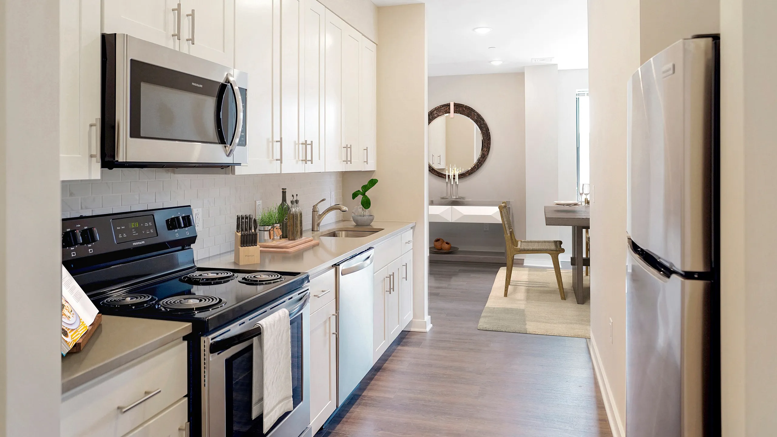 Contemporary kitchen with sleek stainless steel appliances, elegant white cabinetry, and a cozy dining area in the distance.