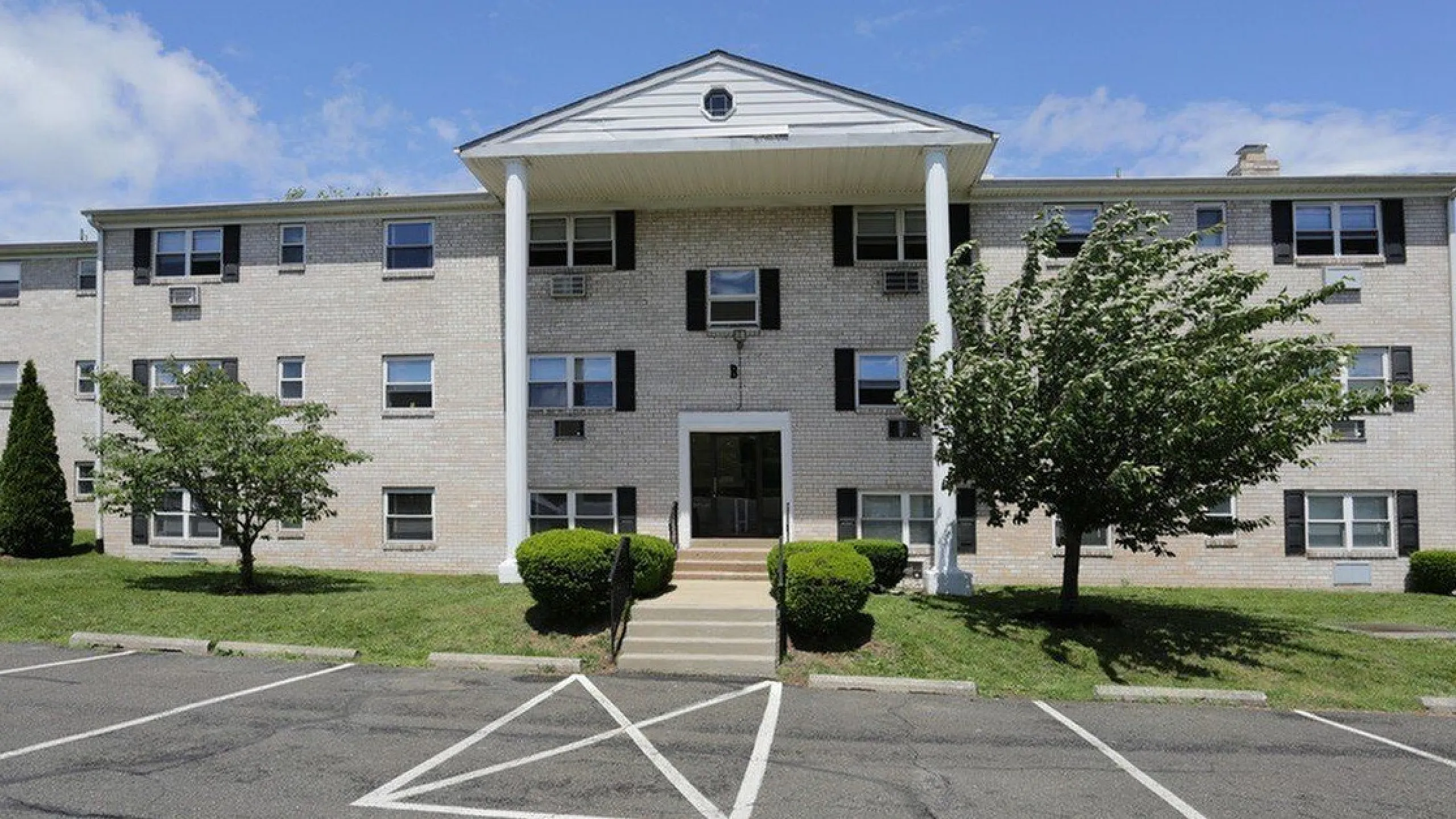 Charming apartment building with classic brick facade, large windows, and lush greenery, perfect for comfortable living.