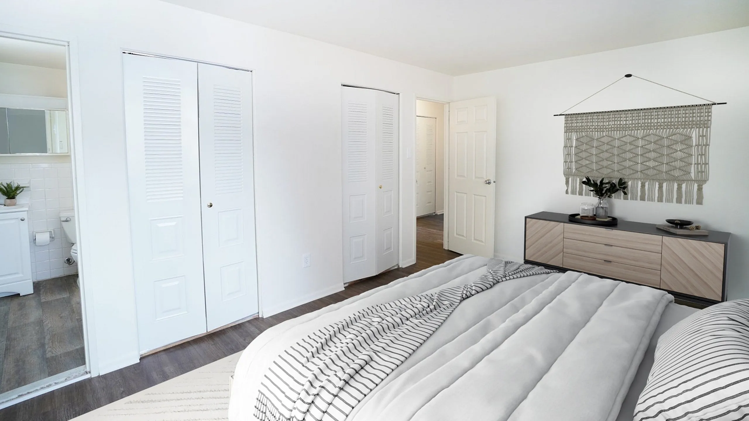 Inviting bedroom with modern decor, featuring a cozy bed, stylish dresser, and a glimpse into a chic bathroom.