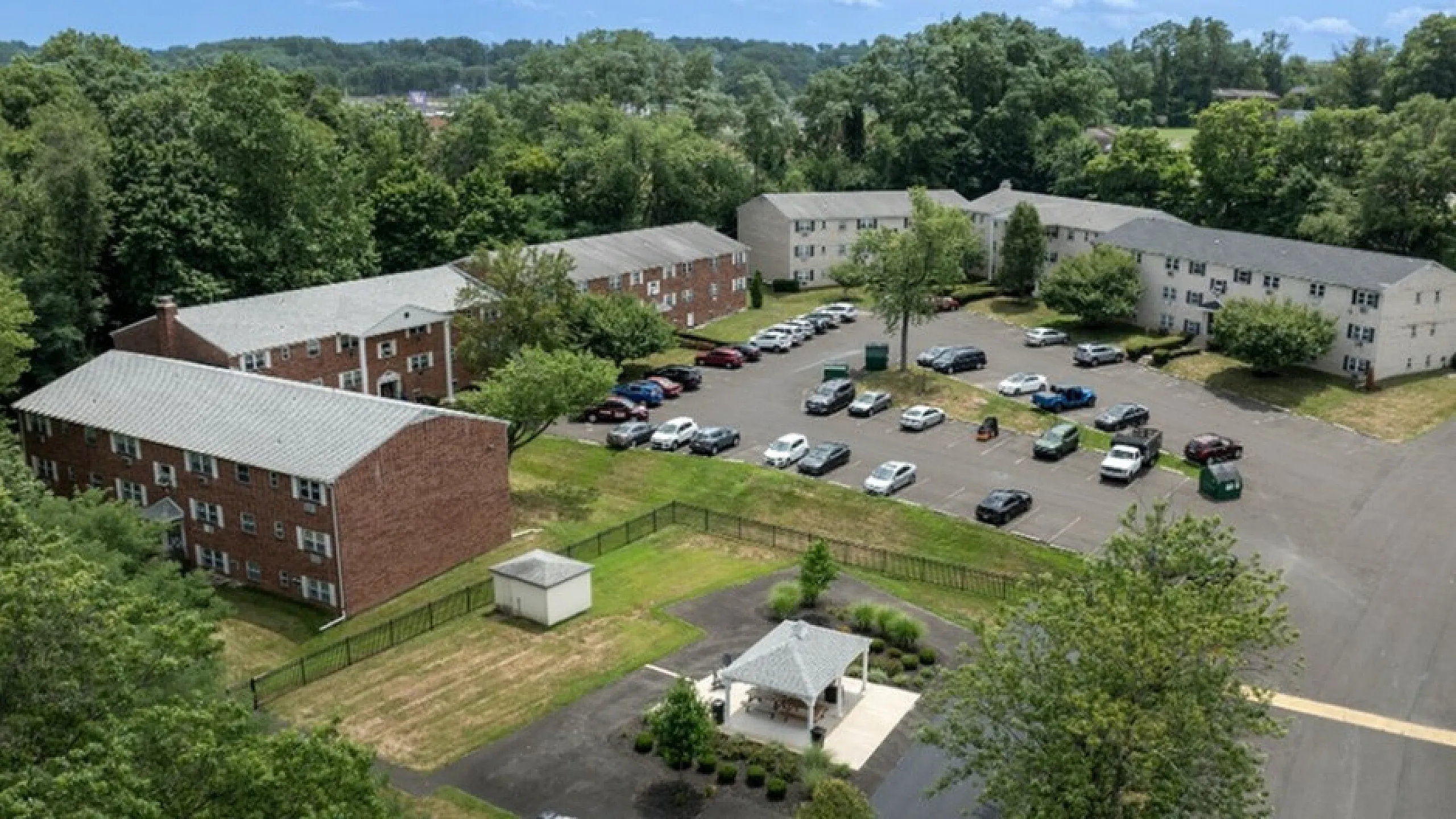 Inviting apartment complex surrounded by lush greenery with ample parking space and charming outdoor seating area.