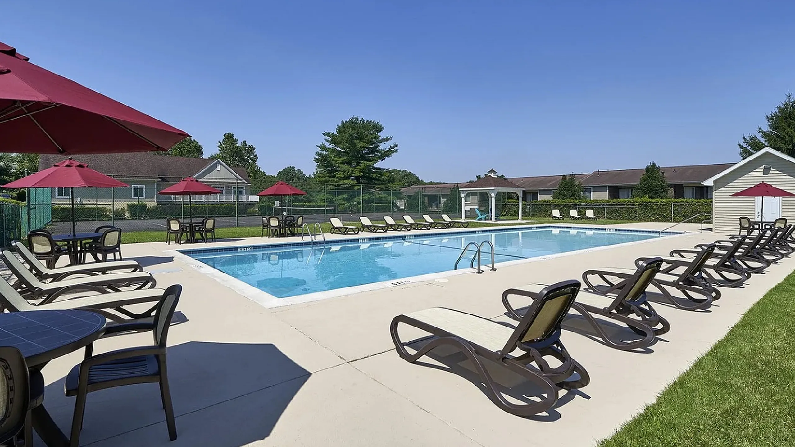 Inviting outdoor pool area with ample lounge chairs and red umbrellas, perfect for relaxation and summer fun.