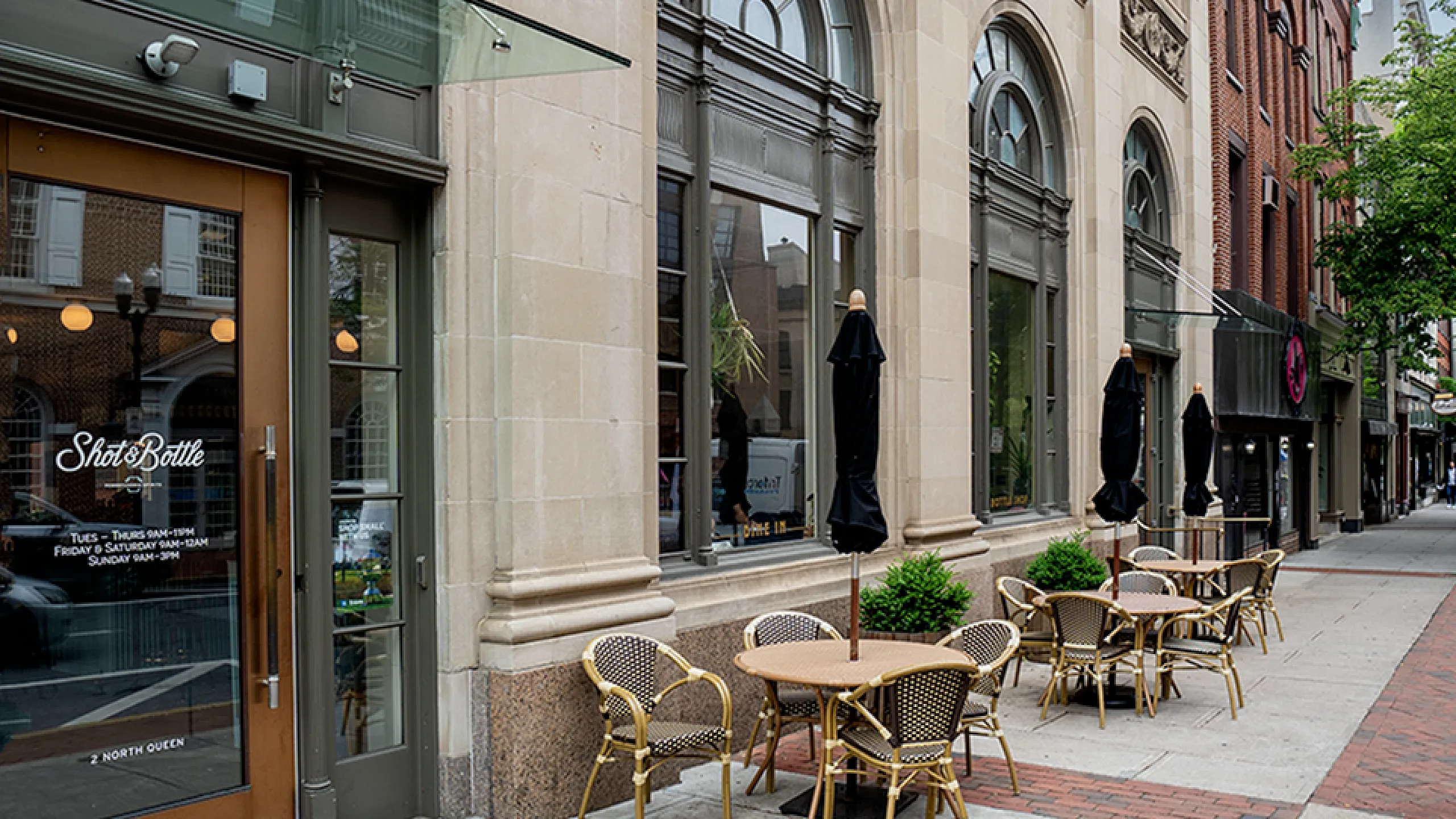 Elegant street-level café with classic architectural design featuring large arched windows, ornate stonework, and inviting outdoor seating.