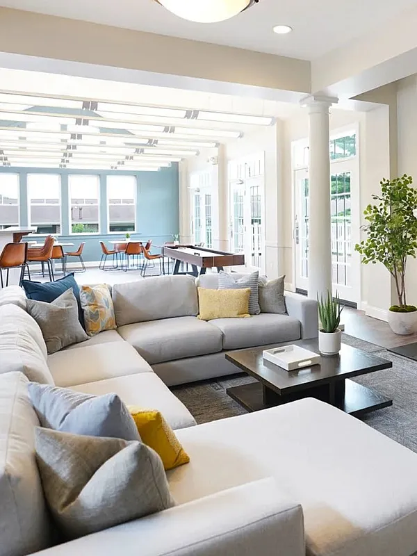 Elegant open-concept living area with large sectional sofa, modern fireplace, and bright dining space under vaulted ceilings, accented by stylish columns and abundant natural light.