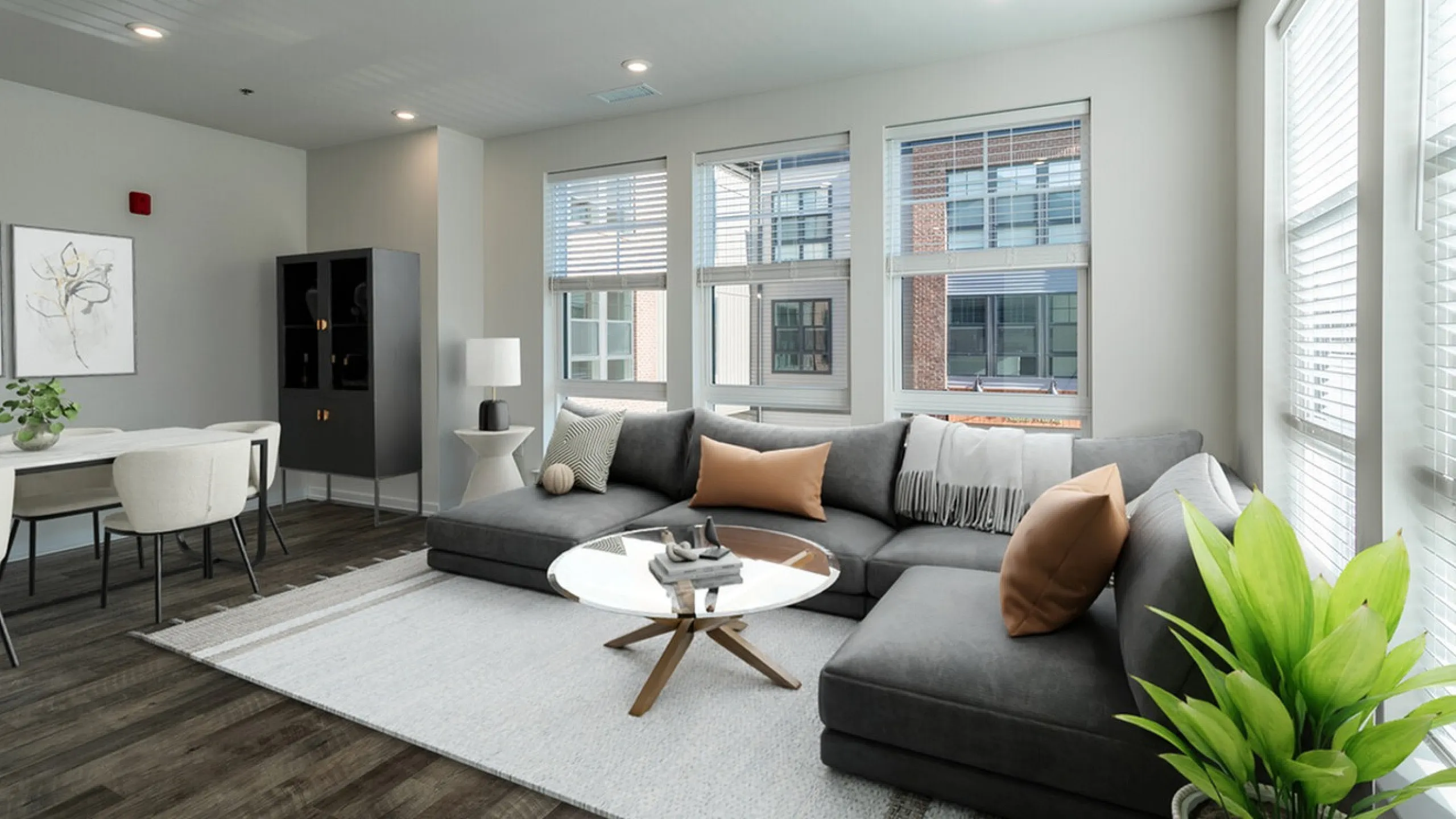 Bright and modern living room featuring a sleek gray sectional sofa, stylish decor, and large windows that flood the space with natural light.