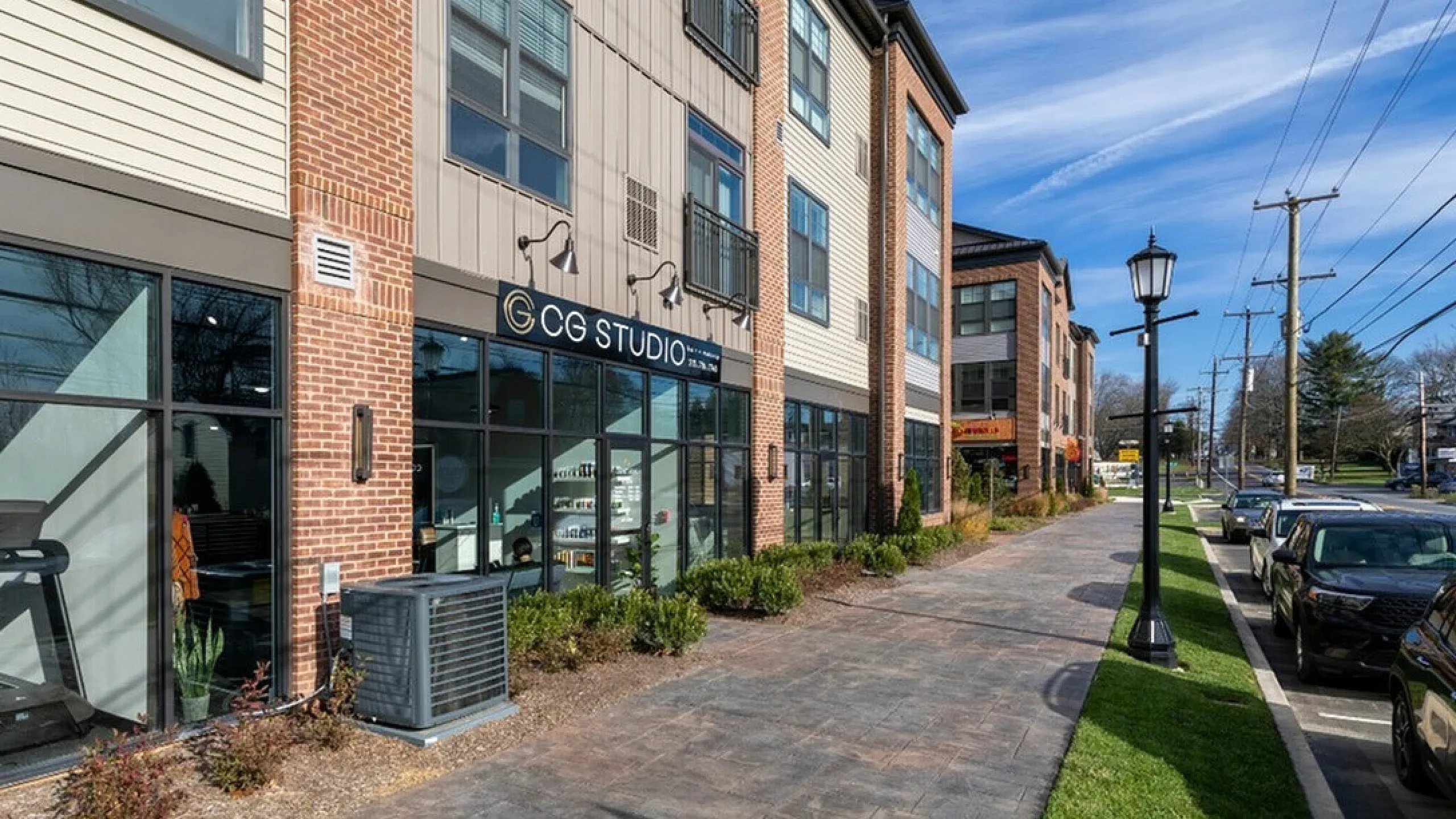 Charming street view of a modern apartment building with large windows and inviting storefronts under a vibrant blue sky.