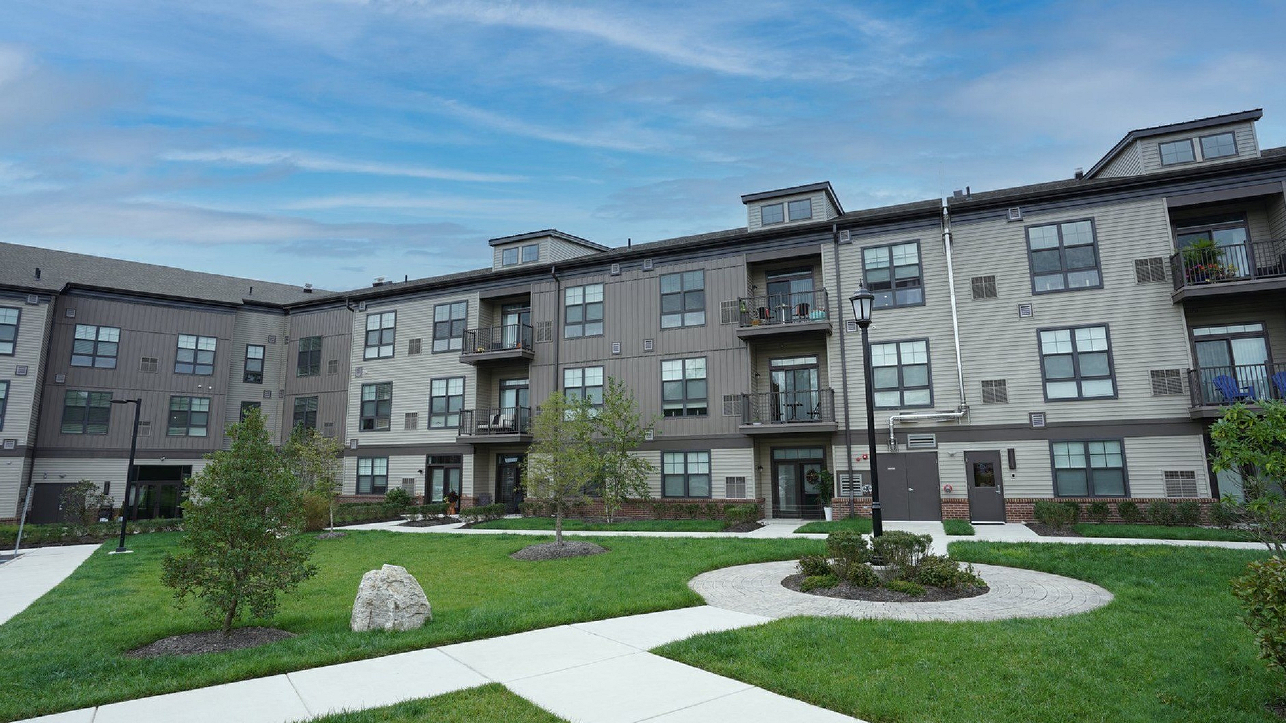 Modern apartment complex with stylish architecture, lush green landscaping, and inviting outdoor pathways under a clear blue sky.