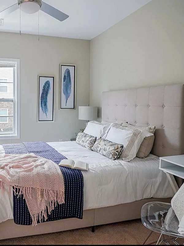 Elegant bedroom with a plush, tufted headboard, cozy bedding, and stylish decor including art pieces and a modern desk.