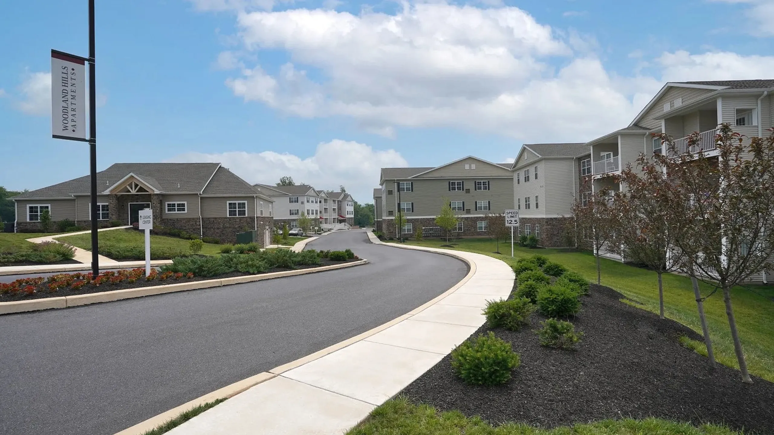 Charming apartment complex surrounded by lush landscaping with a winding road and blue sky backdrop.