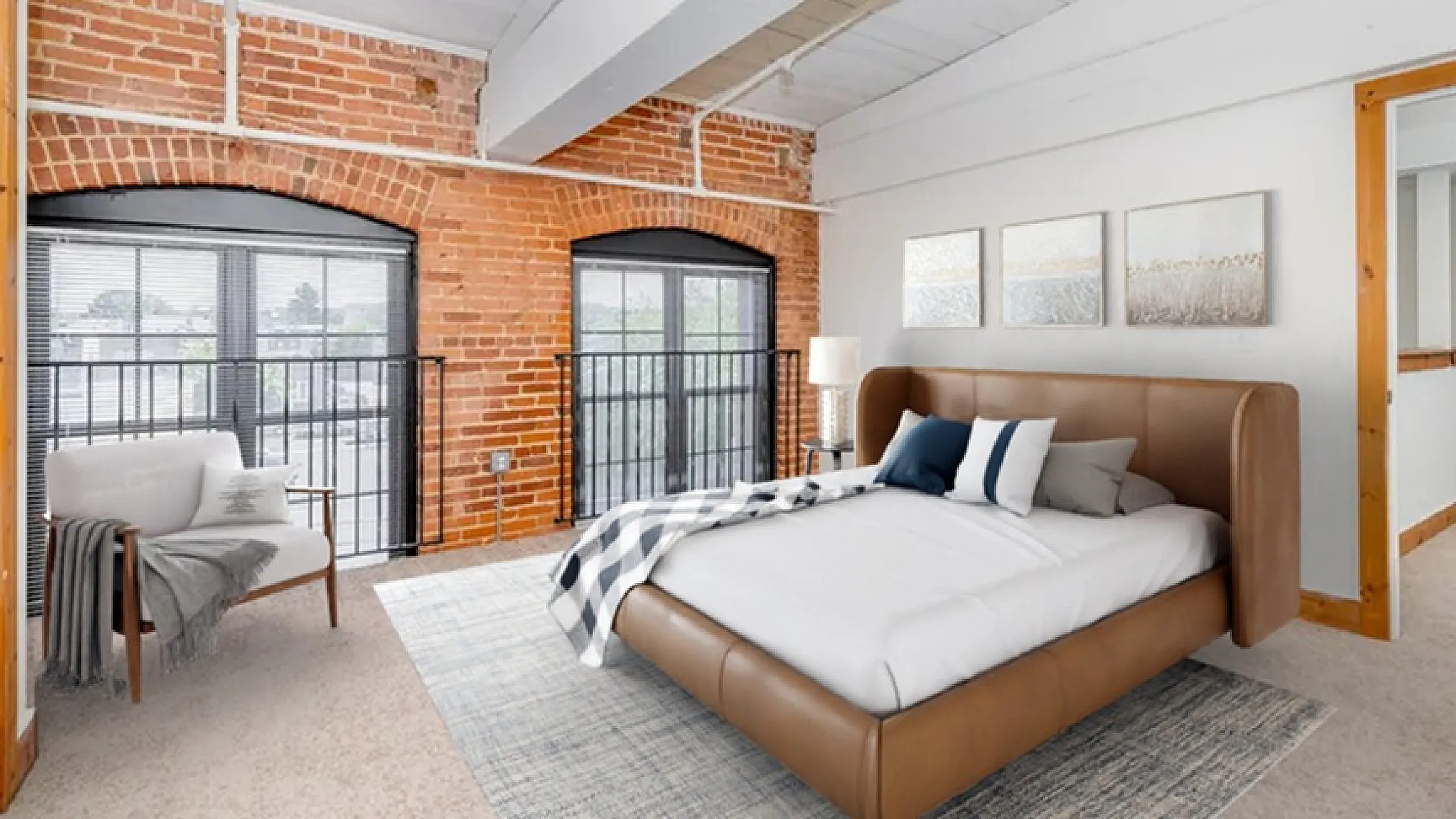 Charming loft bedroom featuring exposed brick walls, elegant decor, and large arched windows with abundant natural light.