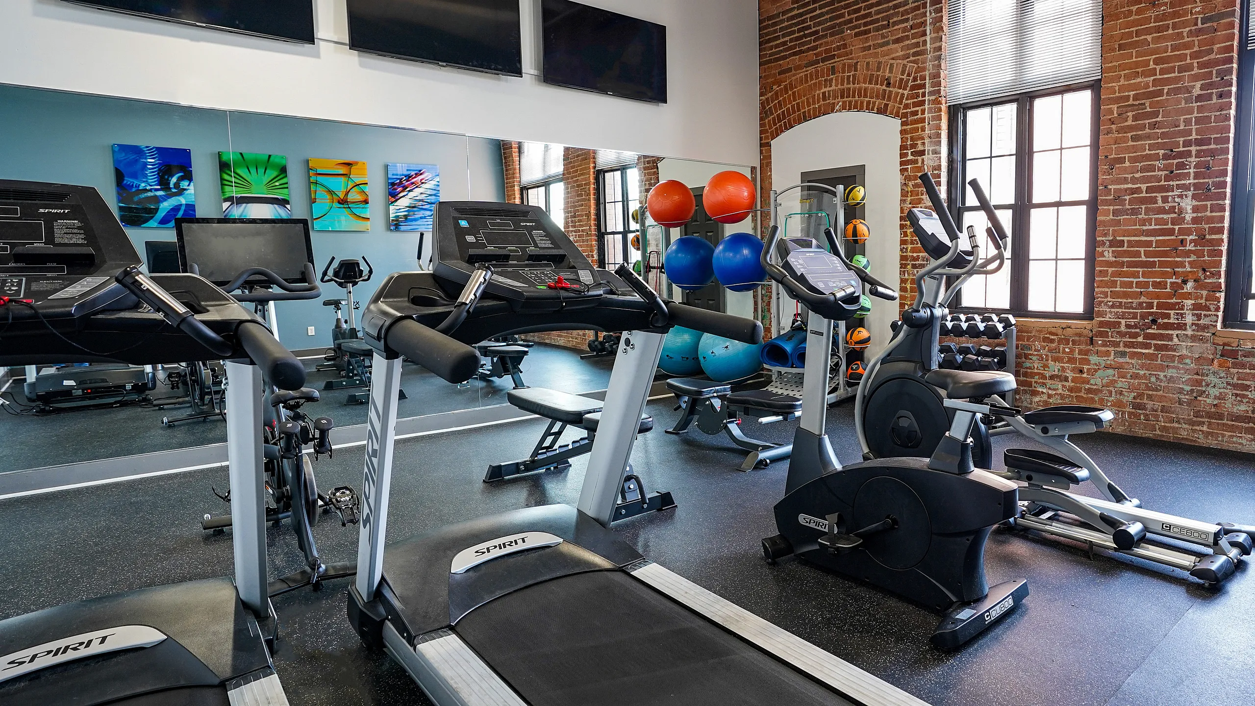 Modern apartment gym with treadmills, exercise bikes, and vibrant artwork, set against stylish exposed brick walls.