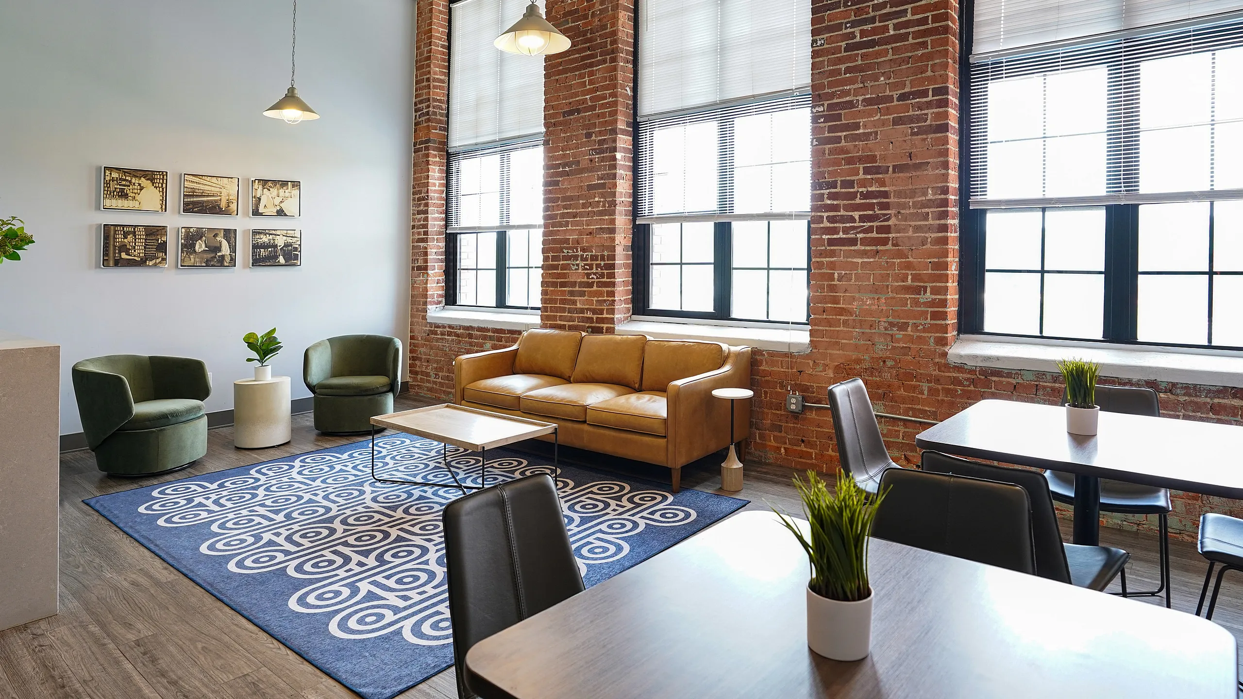 Chic industrial-style living space featuring exposed brick walls, large windows, modern furnishings, and a stylish blue patterned rug.