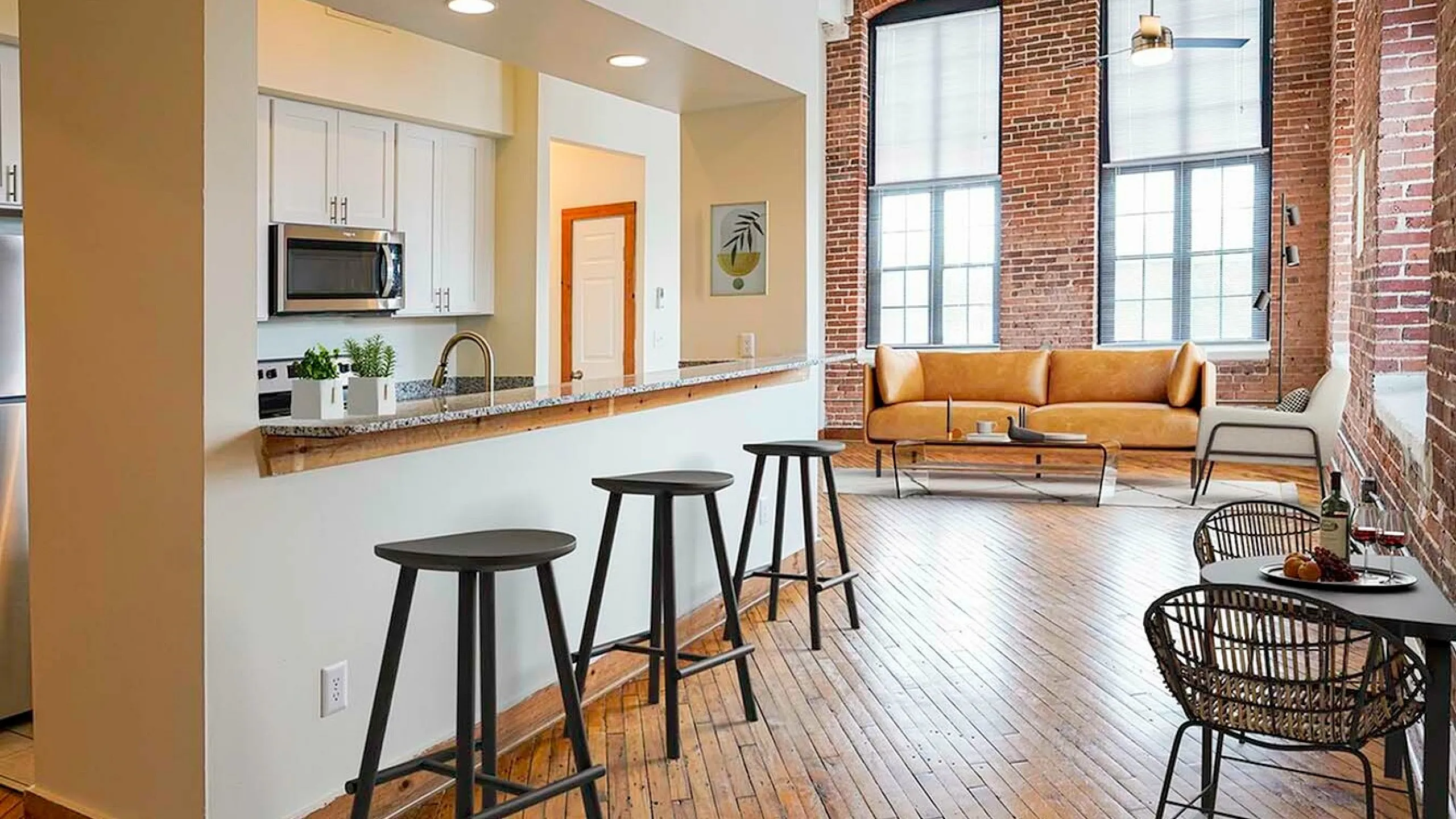 Chic urban apartment with exposed brick walls, featuring a modern kitchen, stylish bar stools, and a cozy living area with ample natural light.