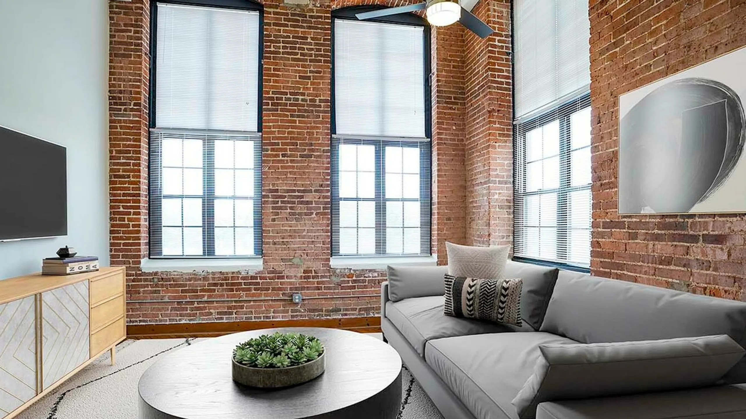 Chic loft-style living room with exposed brick walls, large windows, stylish grey sofa, and modern decor.