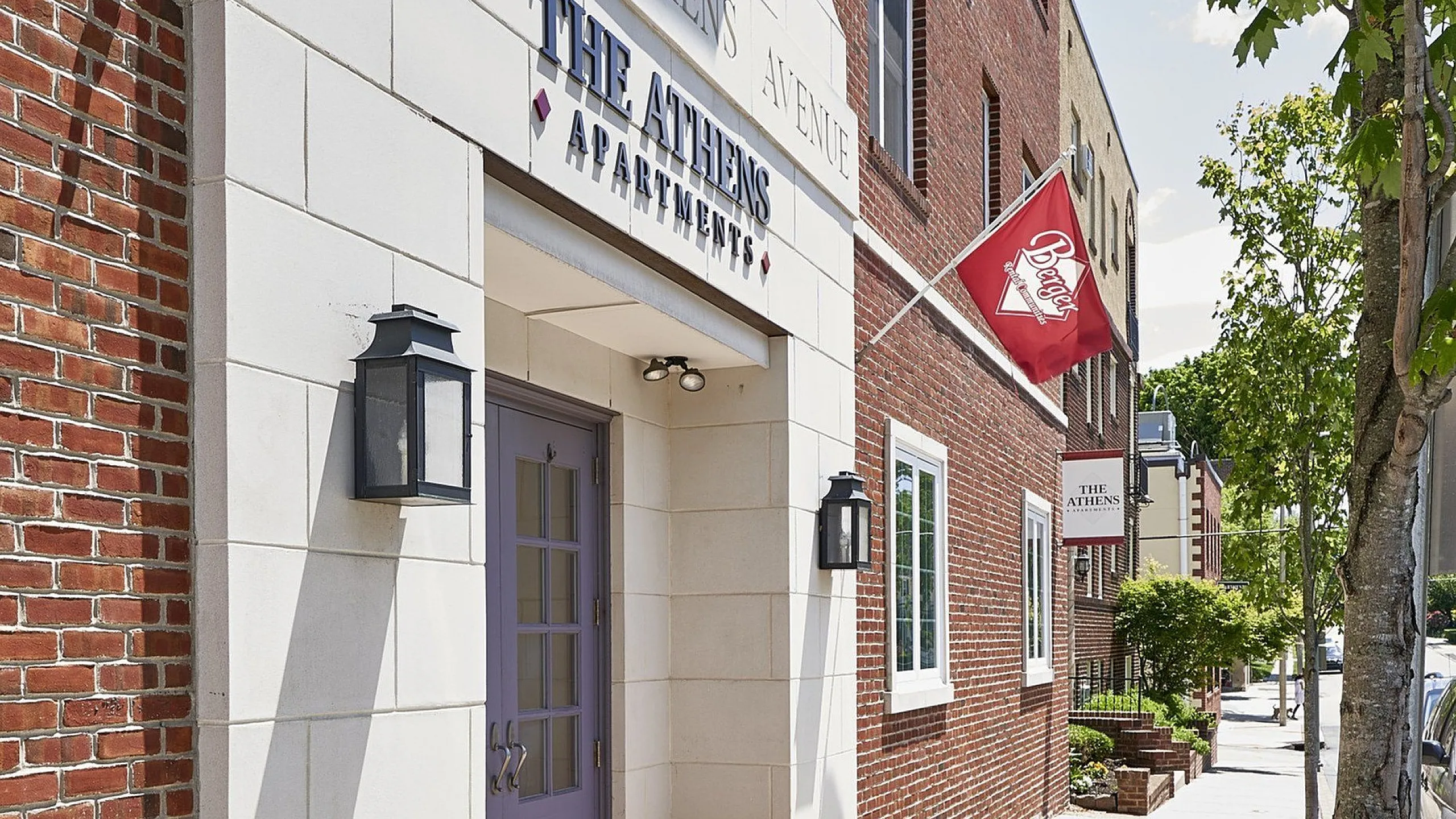 Inviting entrance of The Athens Apartments, featuring elegant brickwork and modern fixtures on a sunny street.