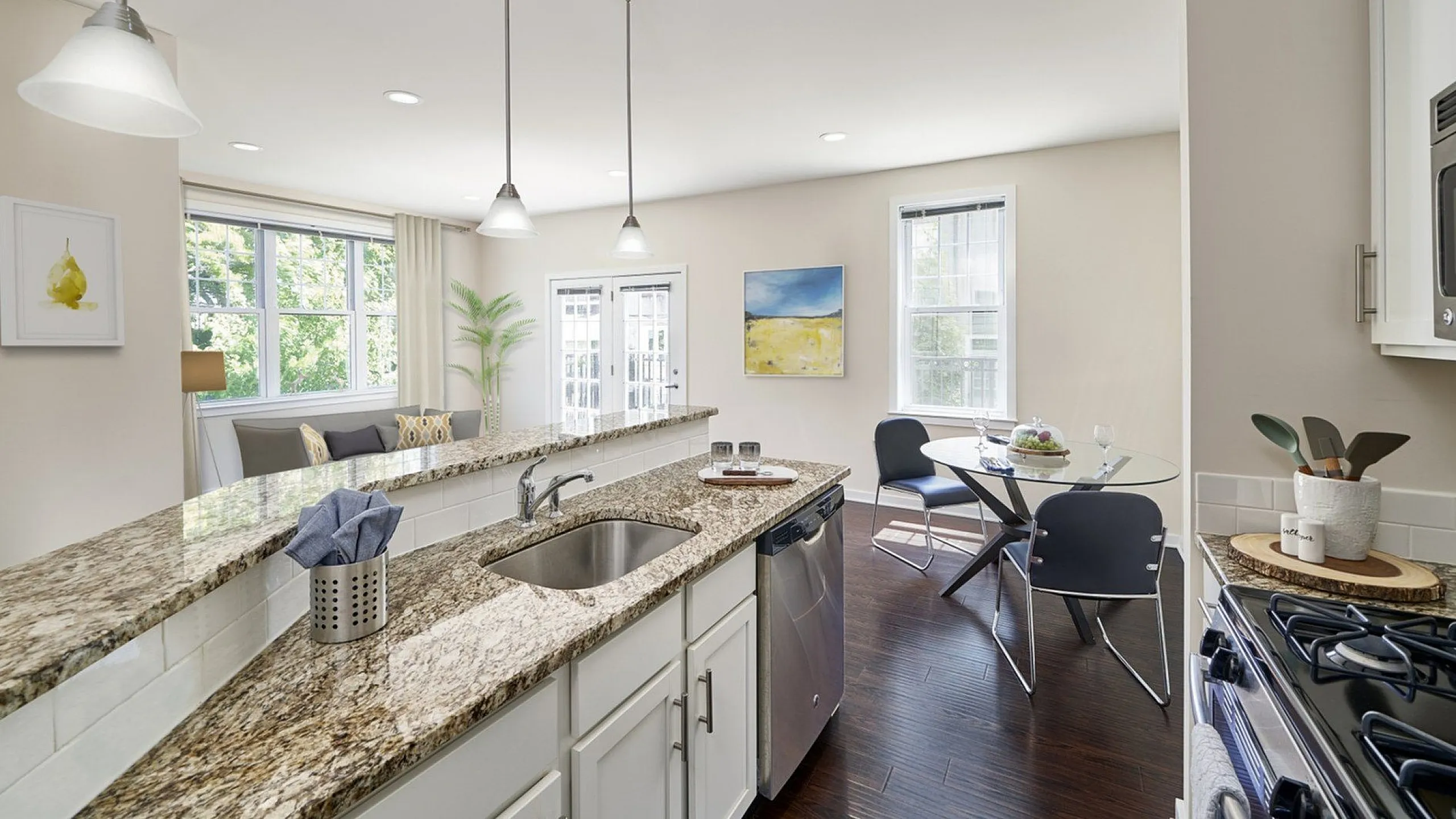 Bright and modern apartment kitchen with granite countertops, pendant lighting, and an open-plan dining area.