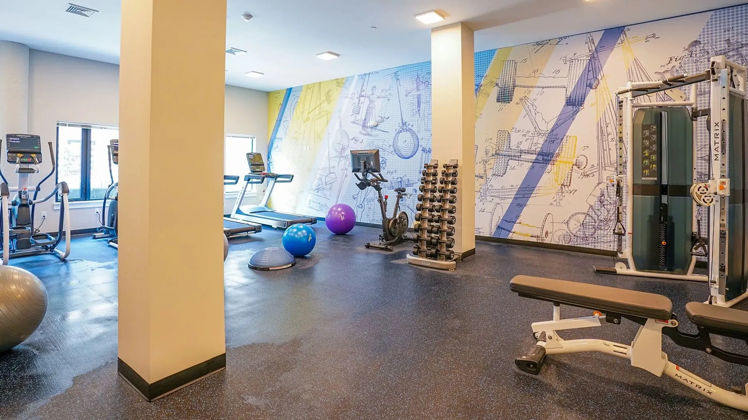 Modern fitness center with state-of-the-art equipment, colorful mural, and ample space for workouts.