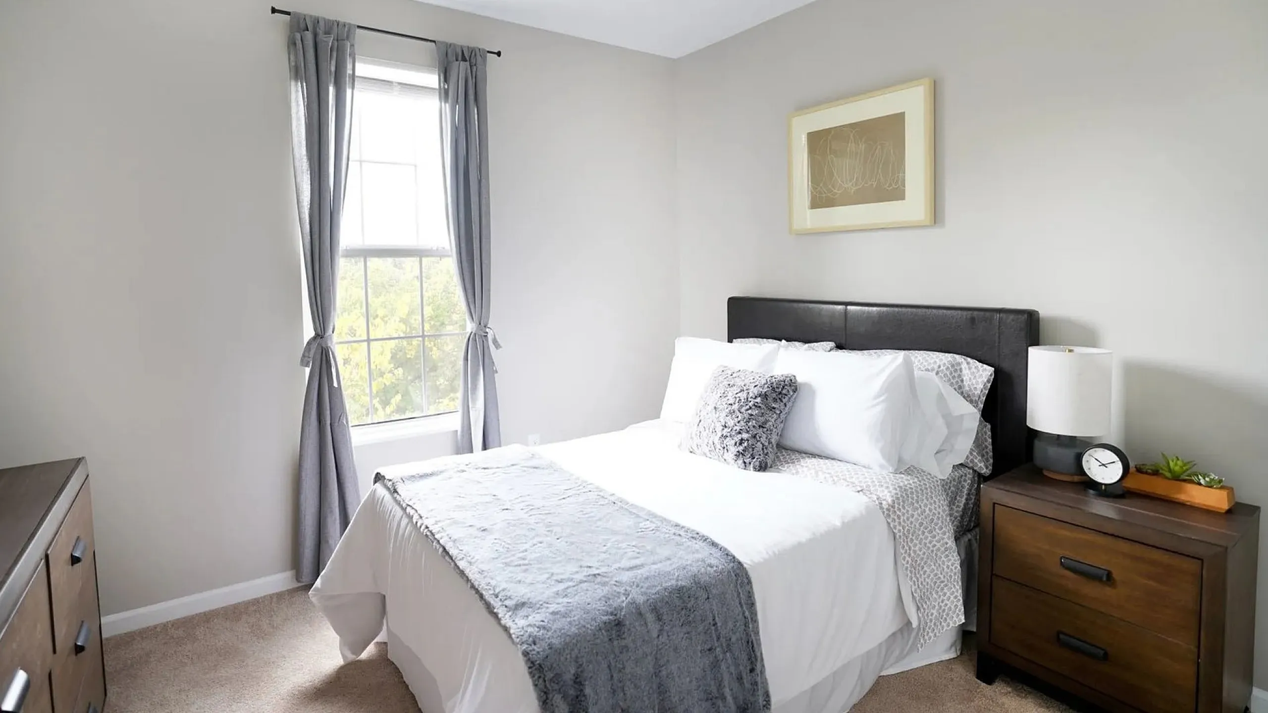 Cozy and bright bedroom with modern decor, featuring a plush bed, elegant nightstand, and large window with soothing natural light.