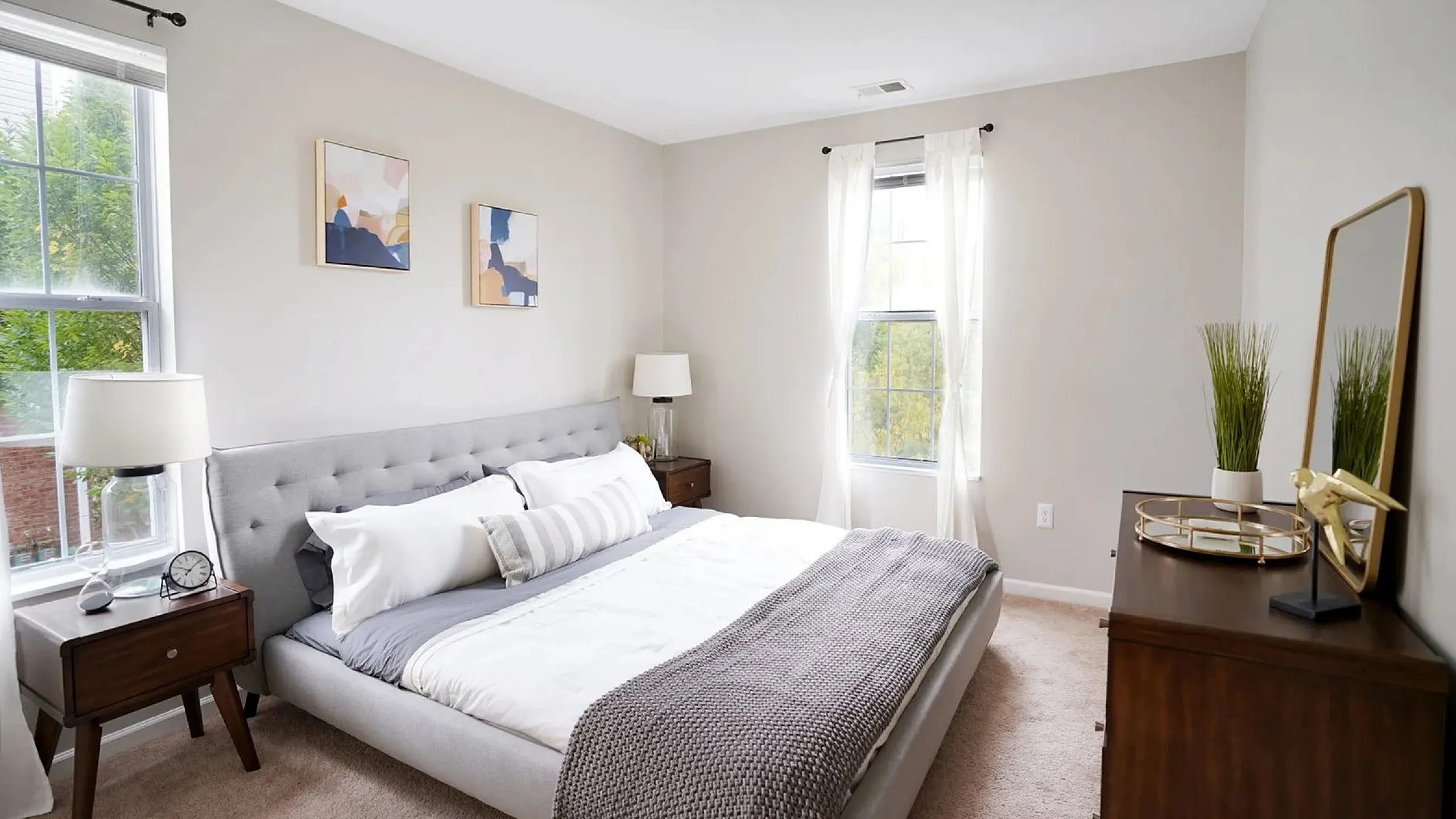 Bright and airy bedroom with a plush gray bed, stylish side tables, and elegant window treatments, perfect for relaxation.