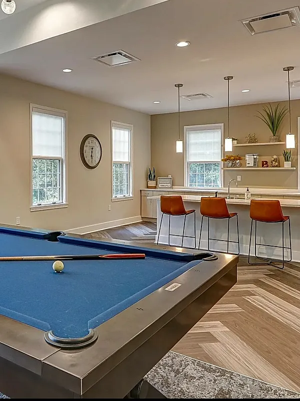 Inviting recreation area with a modern blue pool table, stylish seating, and well-equipped kitchen in a bright, spacious setting.