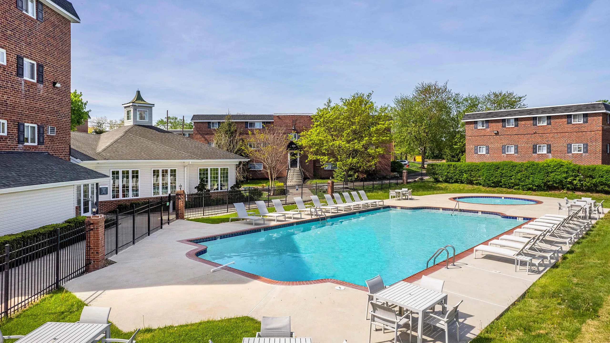 Inviting apartment complex with a sparkling outdoor pool, surrounded by modern lounge chairs and vibrant green landscaping, ideal for relaxation.
