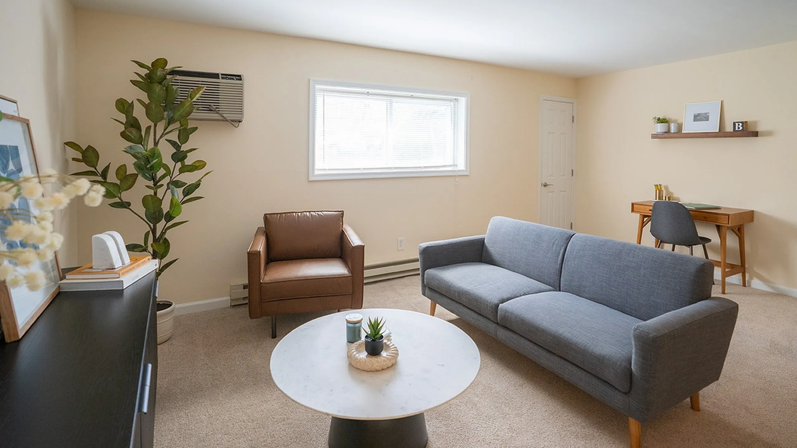 Inviting living room with cozy gray sofa, sleek leather chair, stylish decor, and natural light streaming through the window, creating a warm and contemporary space.