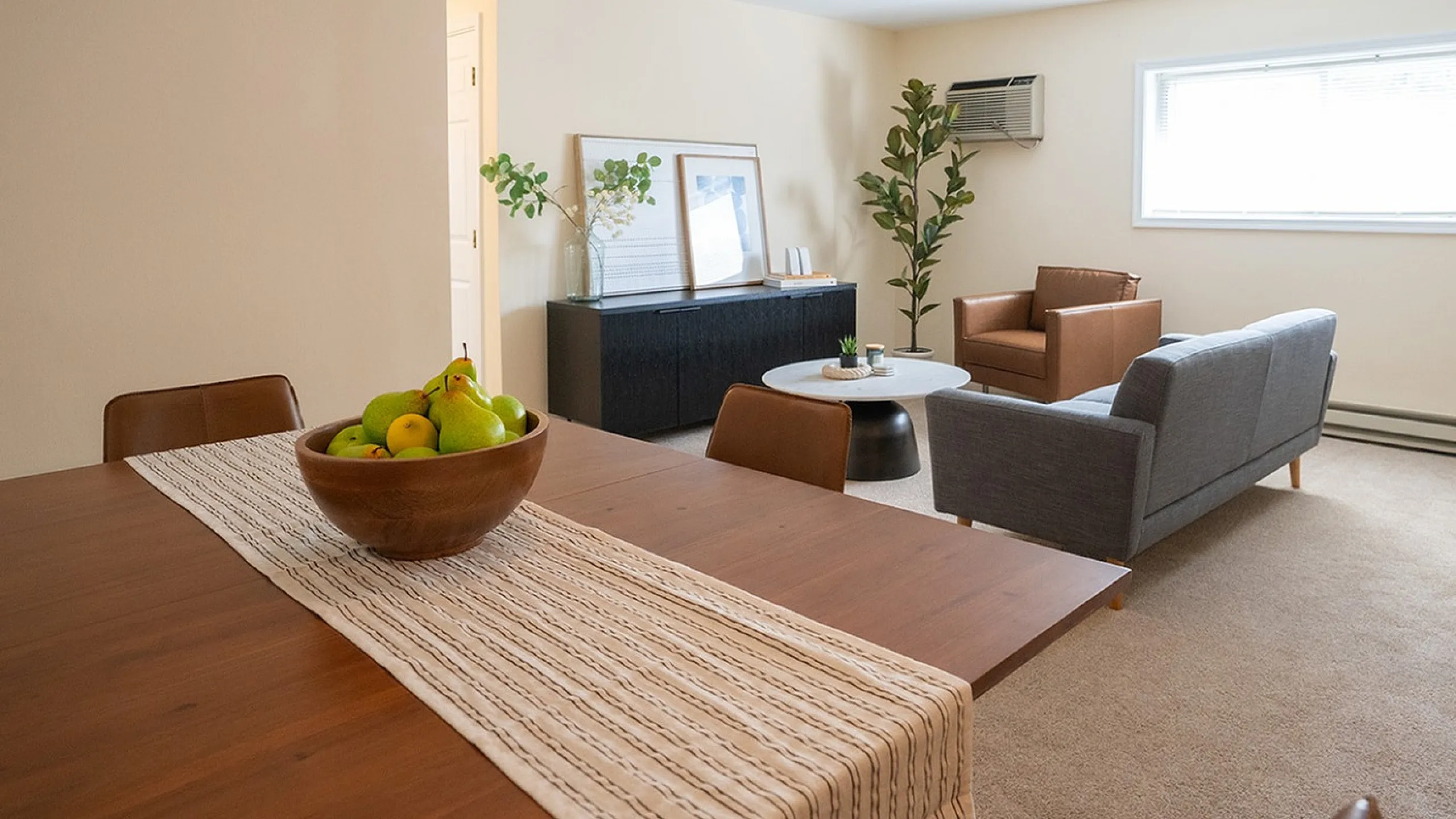 Inviting living room with stylish seating, large window, and cozy dining area with a fruit centerpiece.