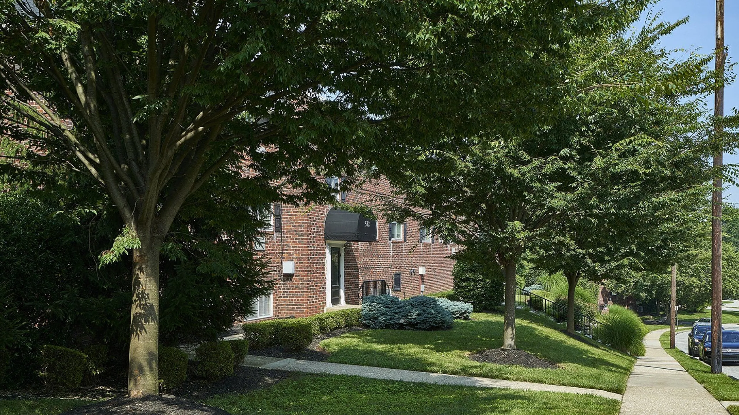 Charming brick apartment complex surrounded by lush greenery and tree-lined sidewalks, offering serene residential living.