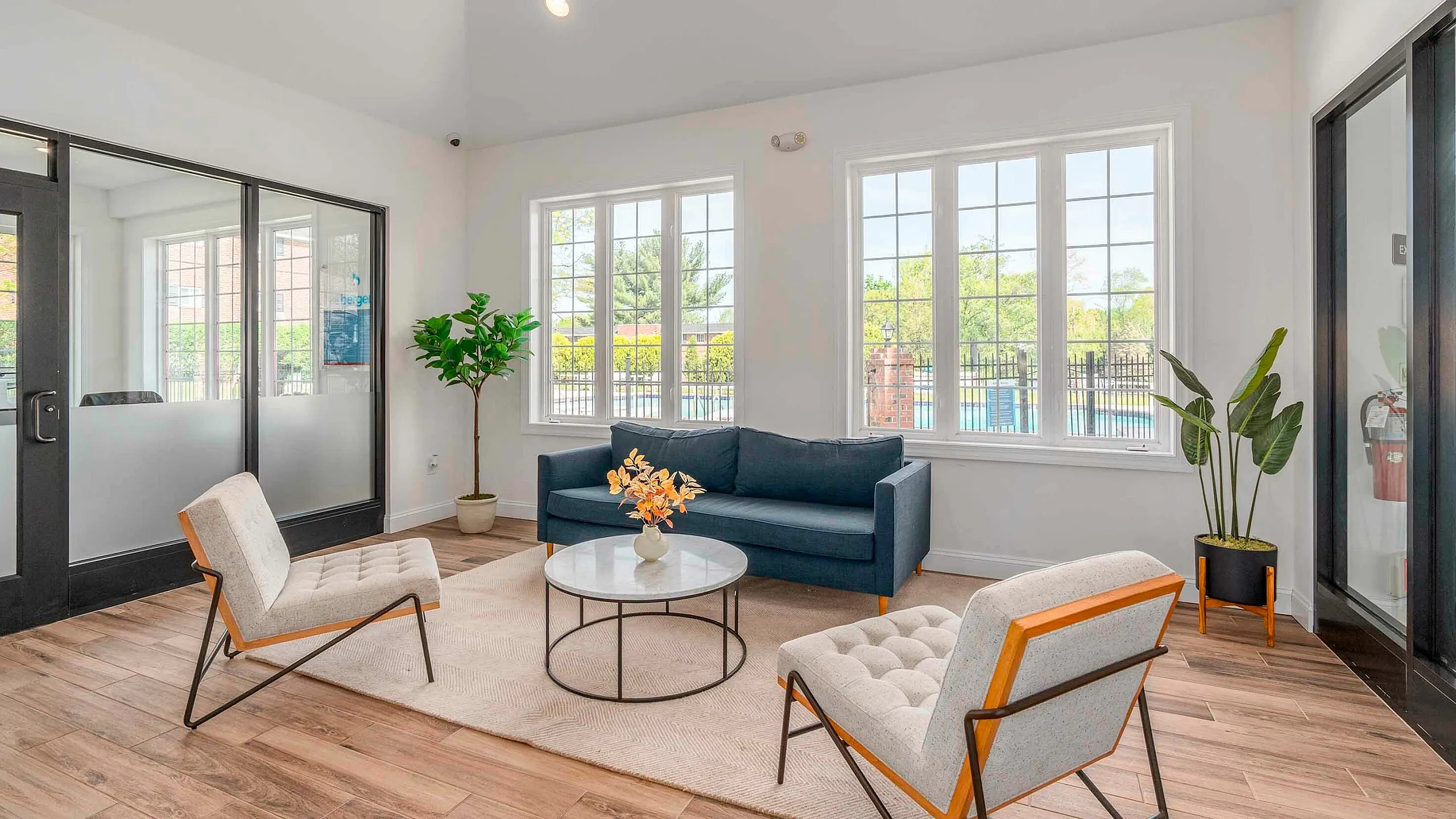 Inviting living room with modern furniture, large windows providing ample natural light, and stylish decor featuring a blue sofa and contemporary chairs.