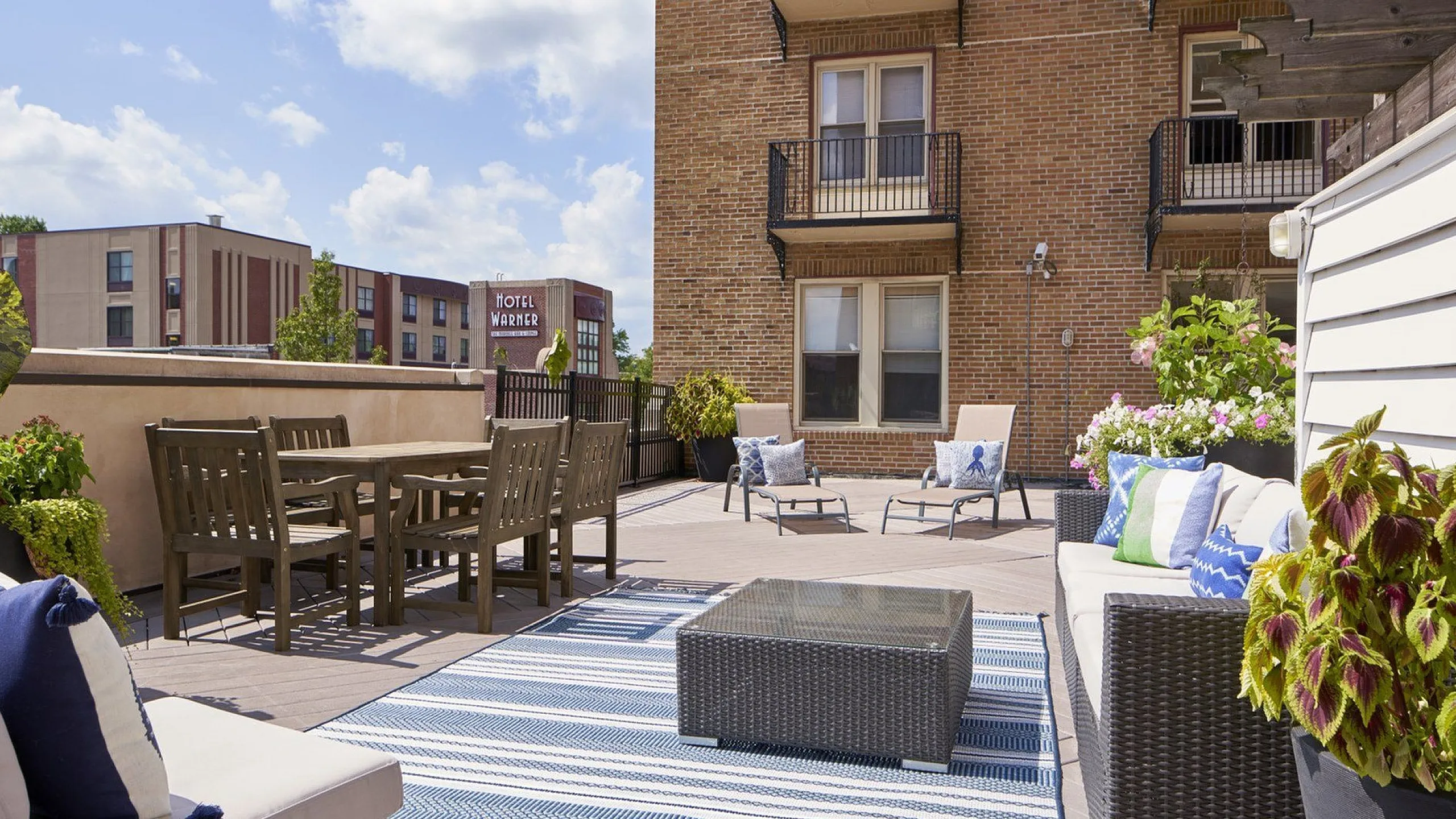 Charming urban terrace with cozy seating, elegant wooden dining set, and vibrant greenery, perfect for relaxation and socializing.