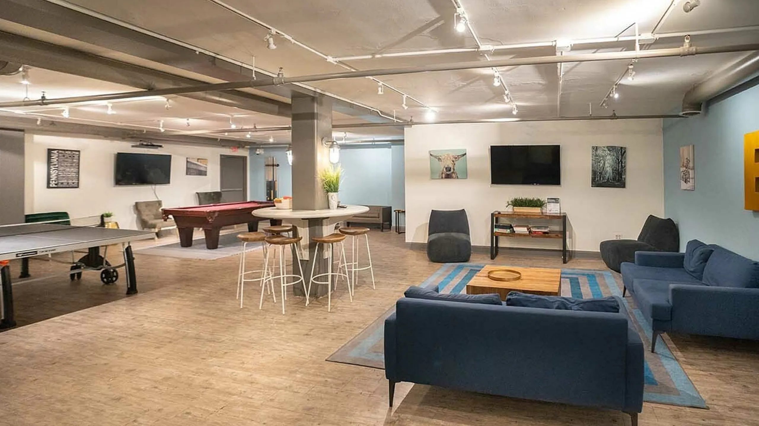 Inviting communal lounge featuring plush blue sofas, a stylish coffee table, game tables, and modern decor for relaxation and entertainment.