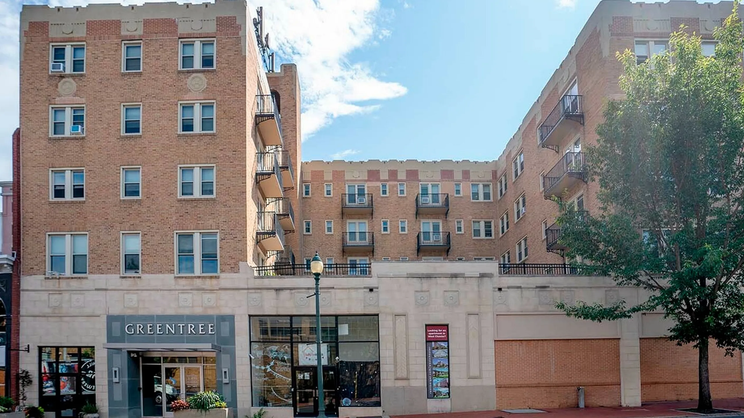 Charming brick apartment complex with a welcoming entrance, set against a bright blue sky.