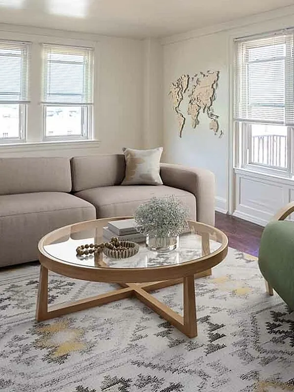 Bright and inviting living room with contemporary decor, featuring a cozy beige sofa, elegant green armchair, and stylish round coffee table on a patterned rug.