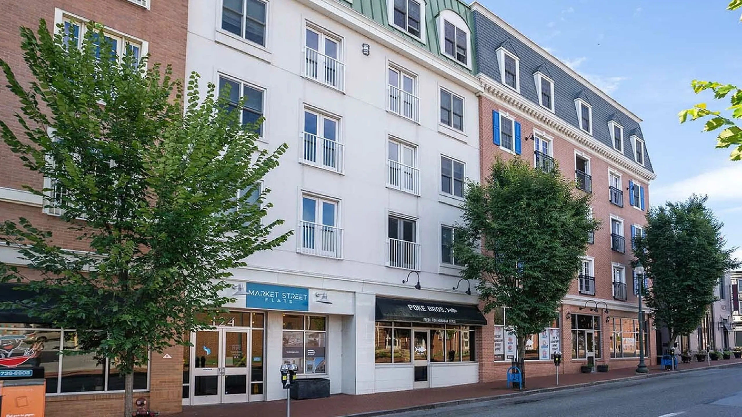 Charming urban apartment complex with modern architecture and street-level retail space, framed by lush greenery.