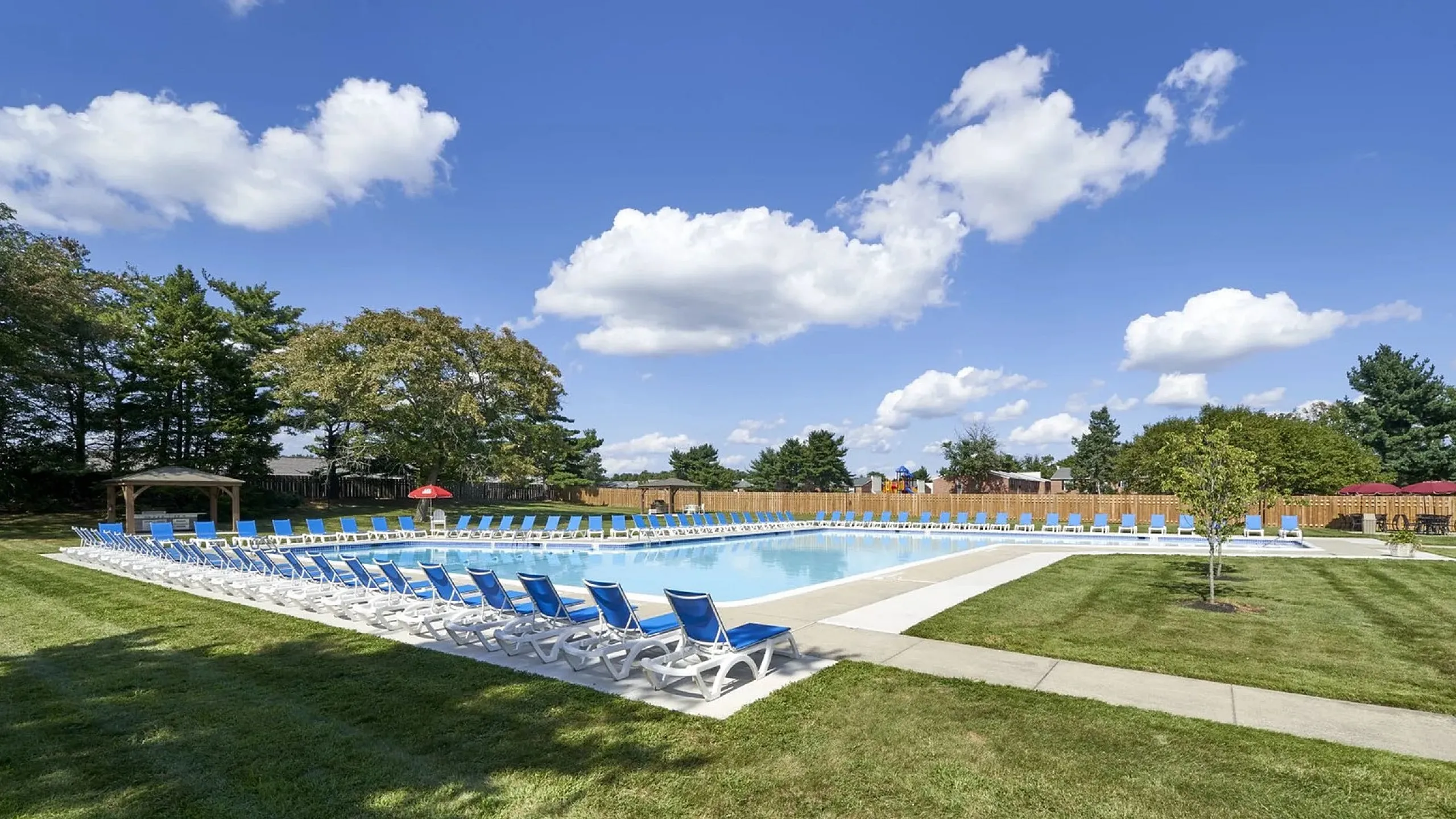 Inviting outdoor pool area surrounded by lush greenery and abundant sun loungers, perfect for relaxation under a vibrant blue sky.