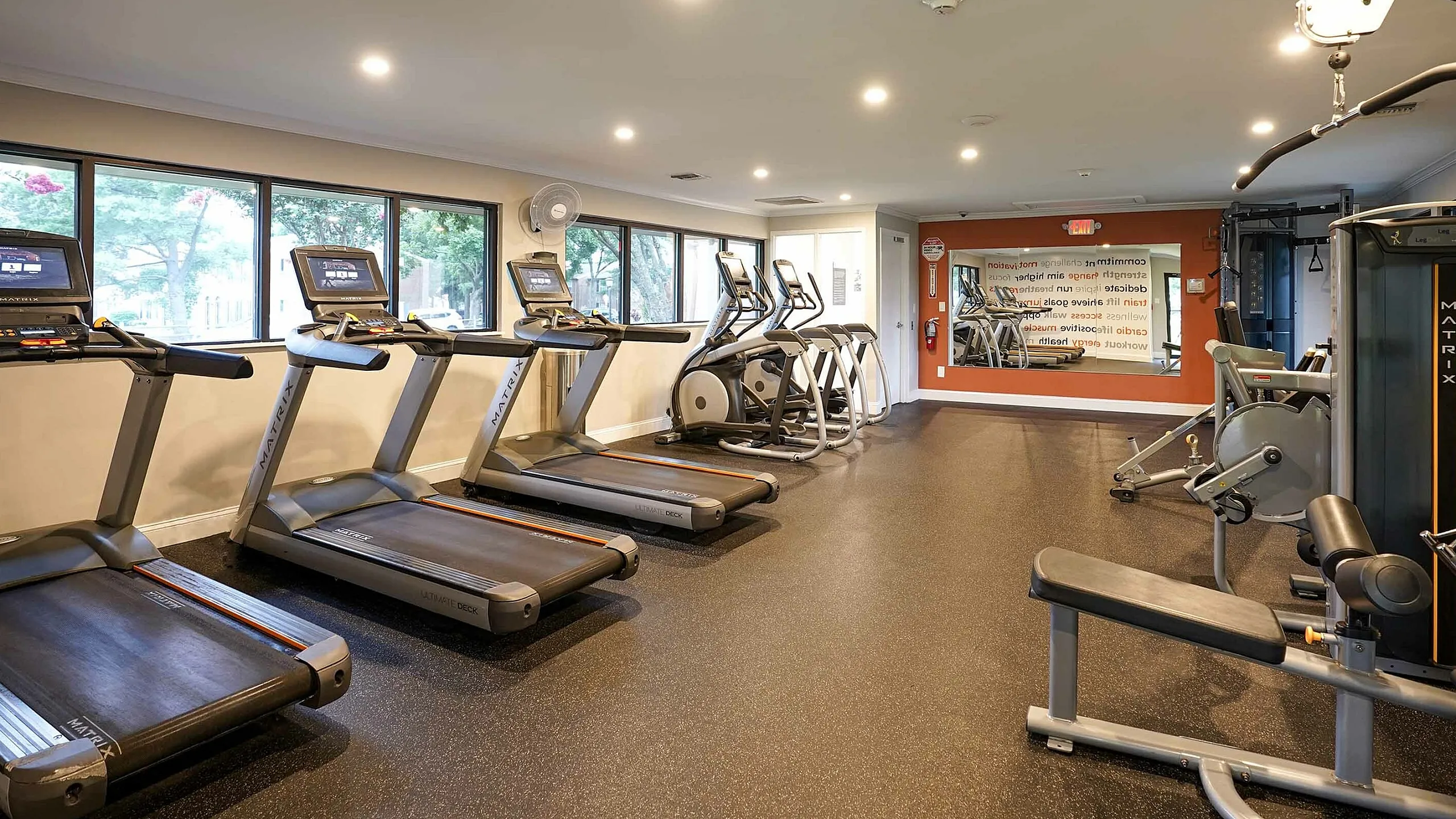 Modern fitness center equipped with state-of-the-art treadmills, elliptical machines, and strength training equipment, featuring large windows and ample natural light.