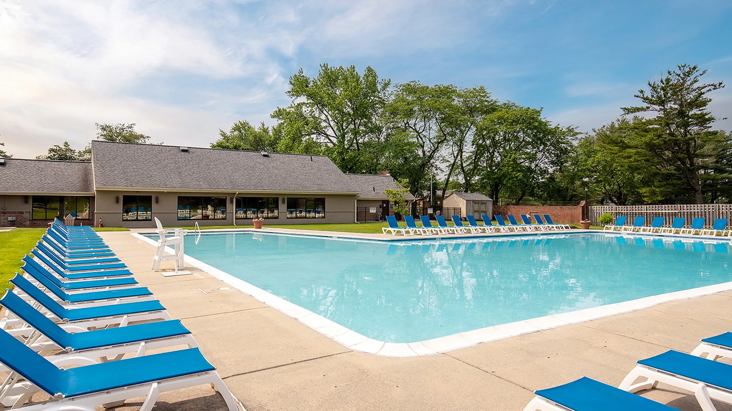 Inviting outdoor pool area with sleek blue lounge chairs and lush greenery, perfect for relaxation and recreation.