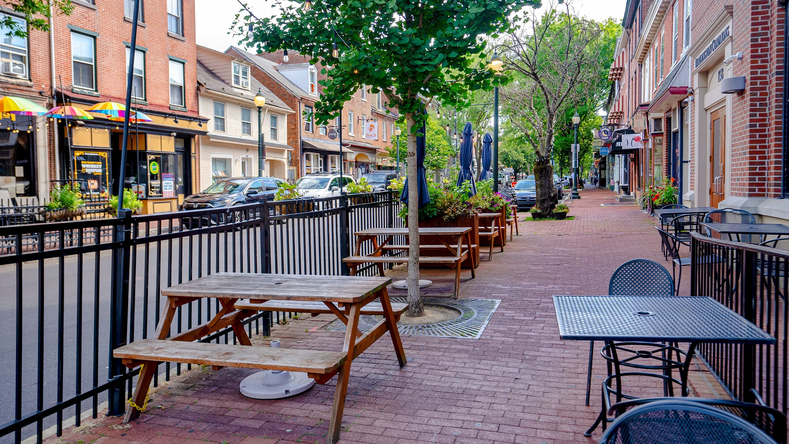 Charming streetscape featuring inviting outdoor seating, vibrant storefronts, and lush greenery, perfect for urban dining and relaxation.