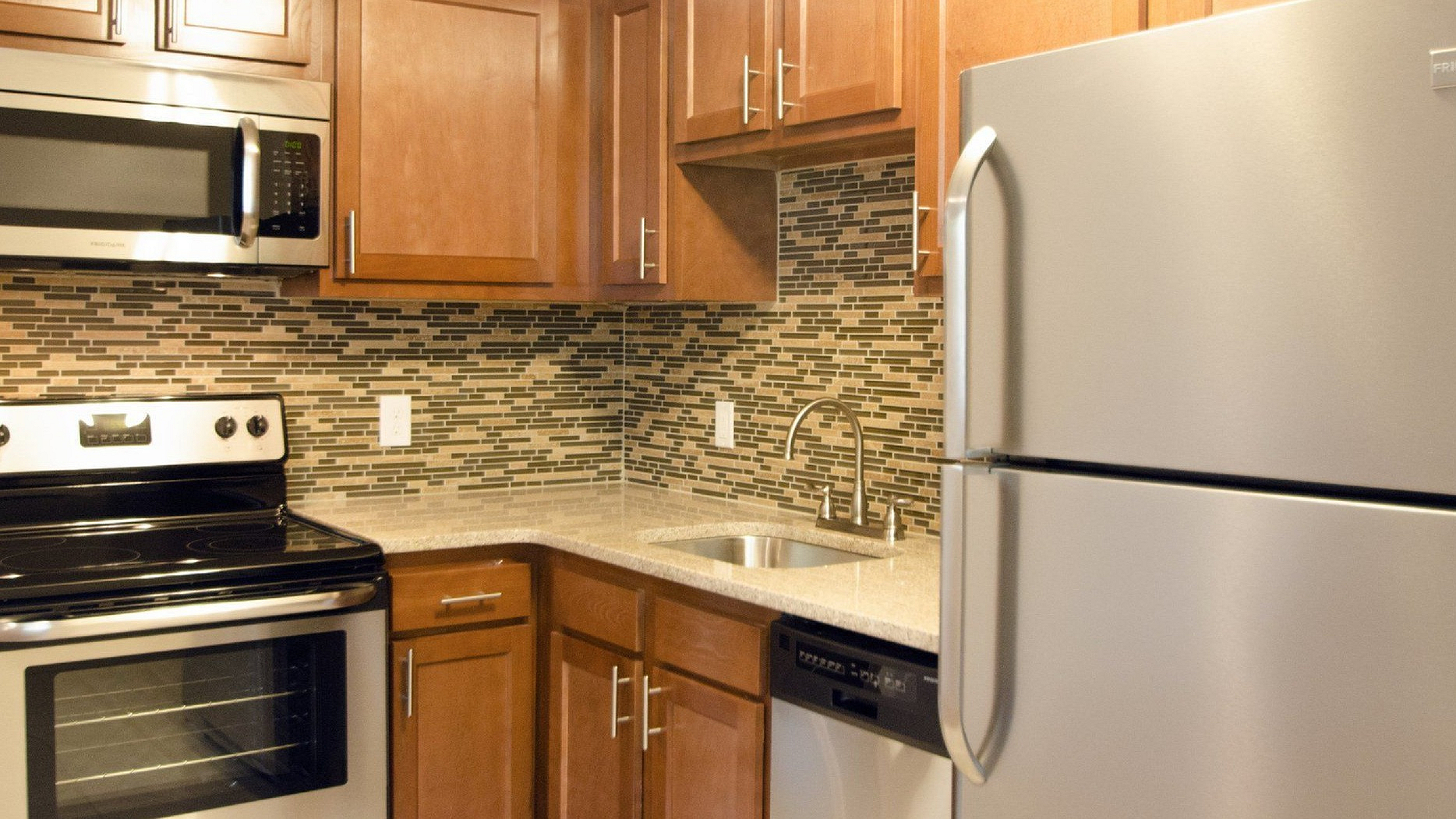 Modern kitchen with sleek stainless steel appliances, elegant wooden cabinets, and stylish mosaic backsplash.