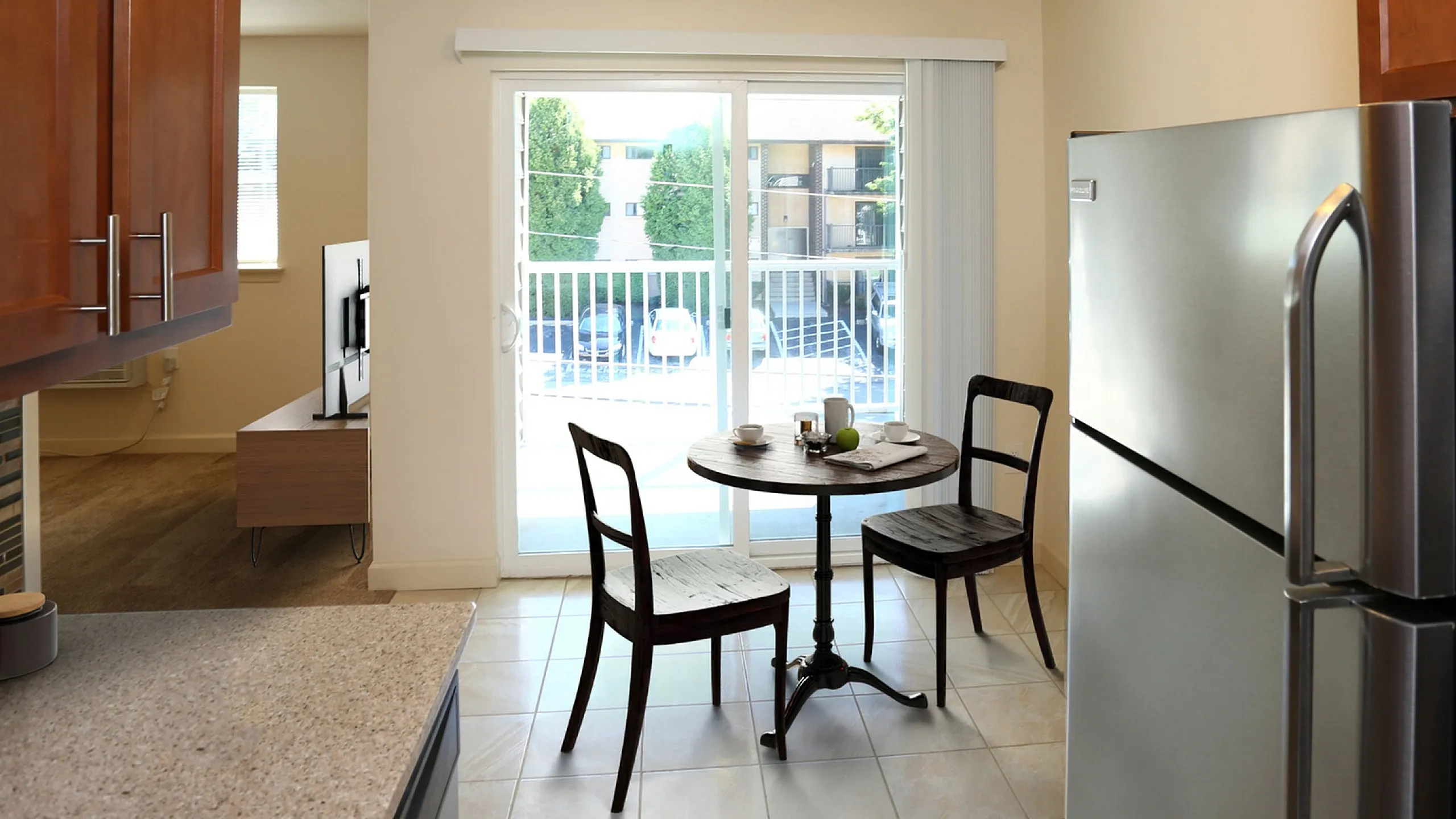 Charming kitchen area with sleek stainless steel fridge, cozy dining nook, and natural light streaming through sliding glass doors opening to a balcony view.