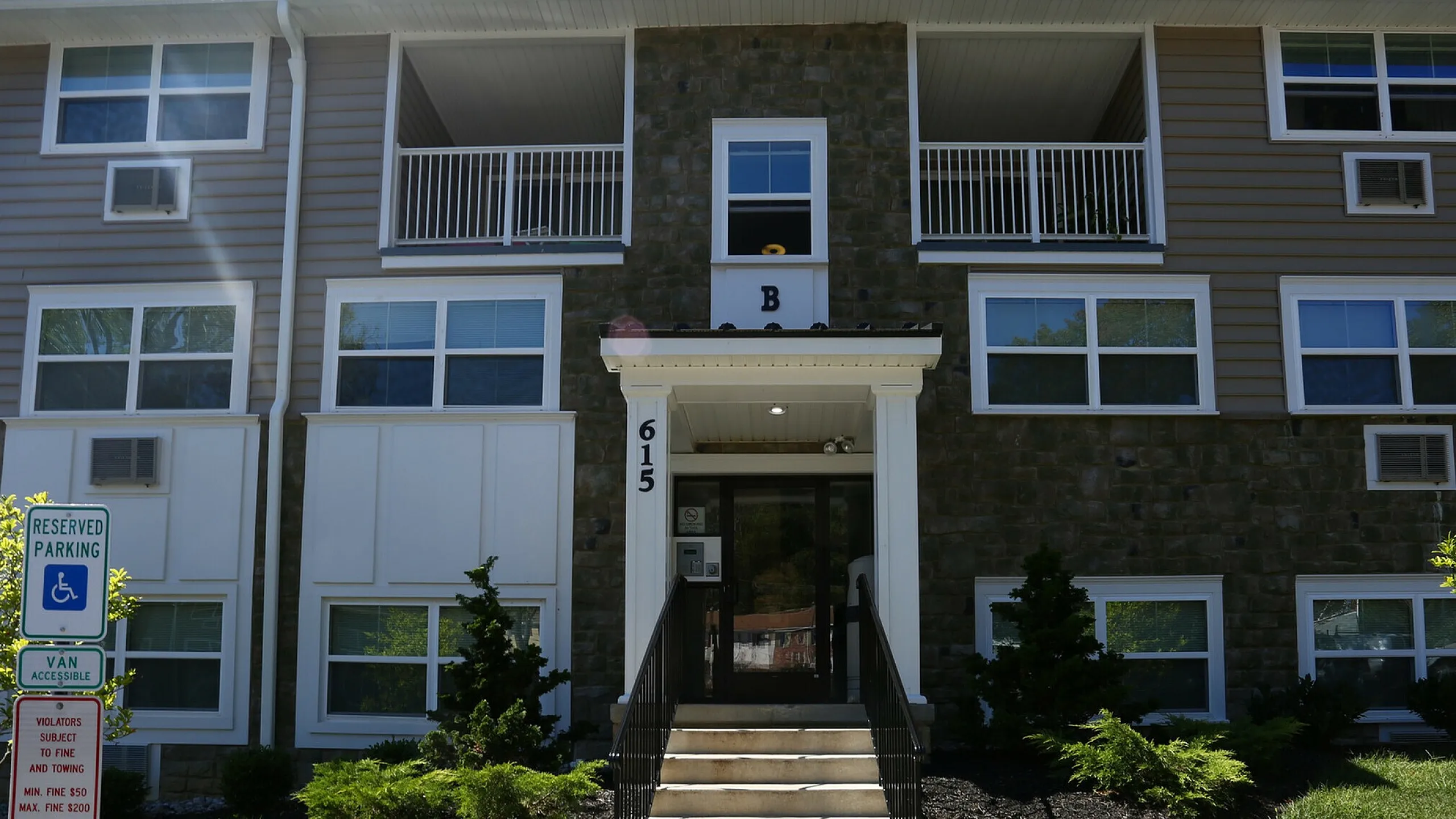 Charming apartment building featuring modern stone facade, lush landscaping, and accessible entry.