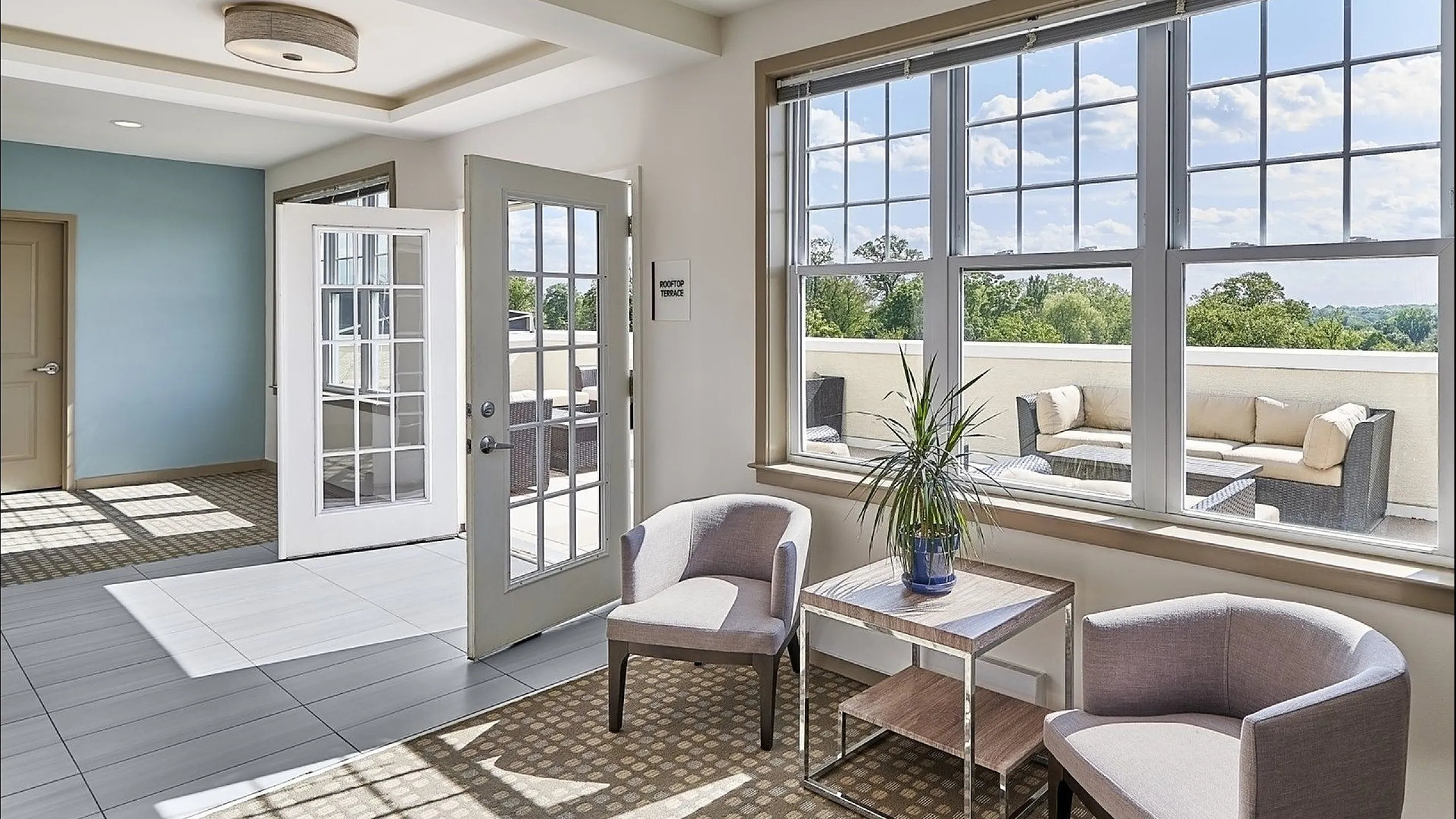 Bright lounge area with plush armchairs, large windows overlooking a scenic view, and direct access to a rooftop terrace.