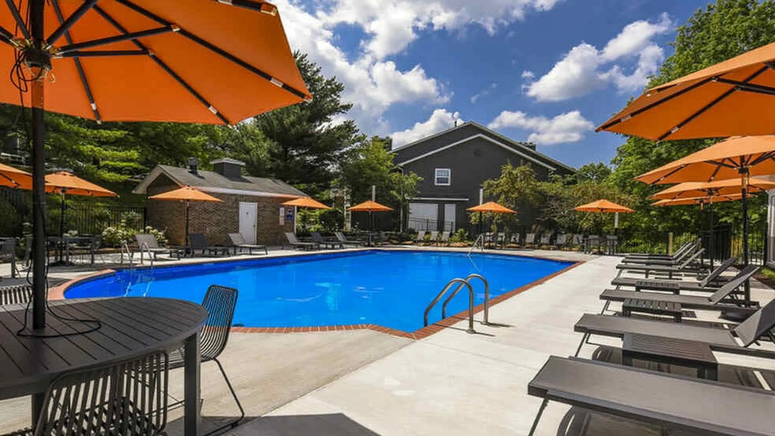 Inviting outdoor pool area with vibrant orange umbrellas and comfortable loungers, perfect for relaxation under a sunny sky.