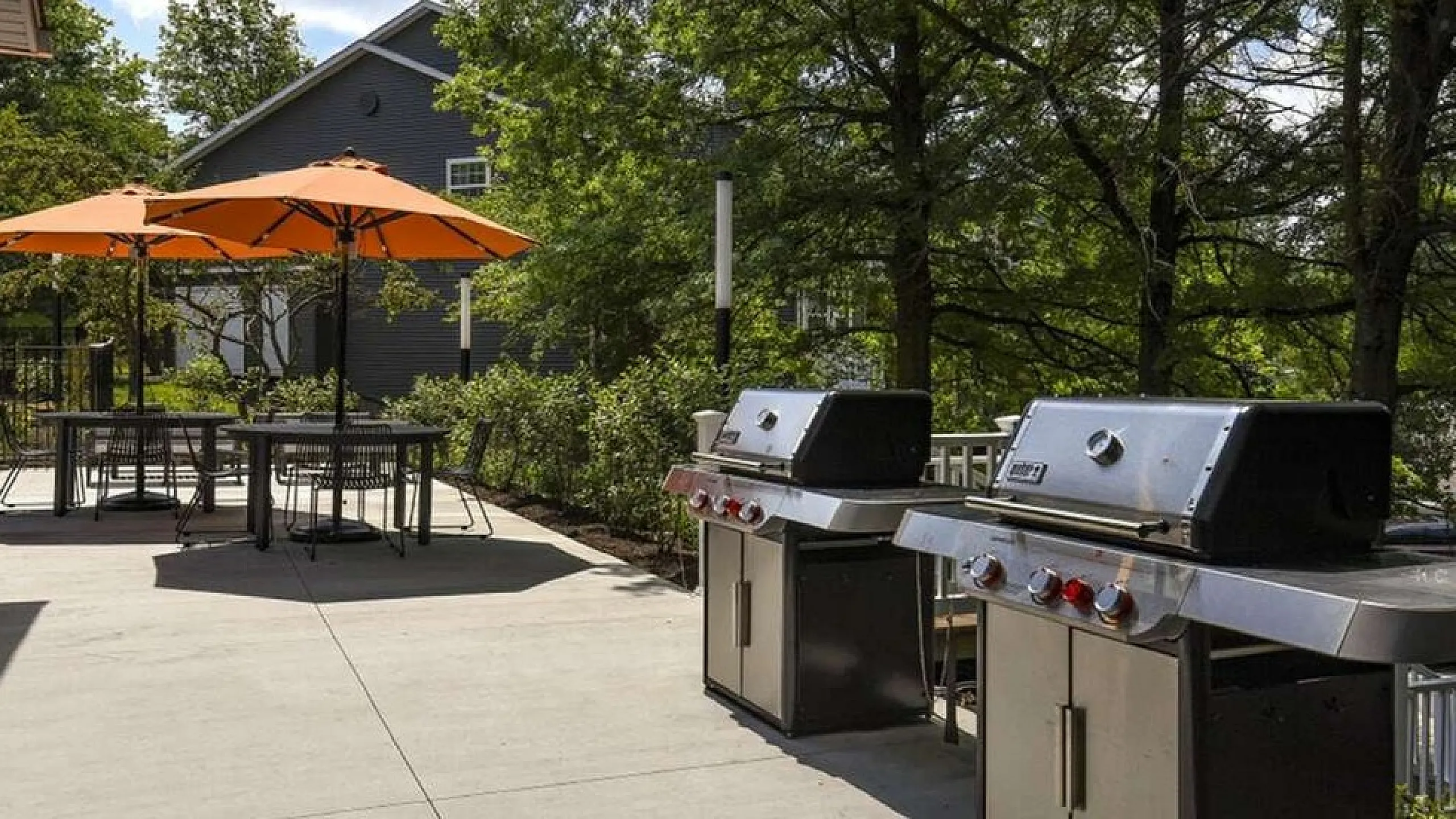 Chic outdoor patio with barbecue grills and vibrant orange umbrellas, perfect for entertaining and relaxation.