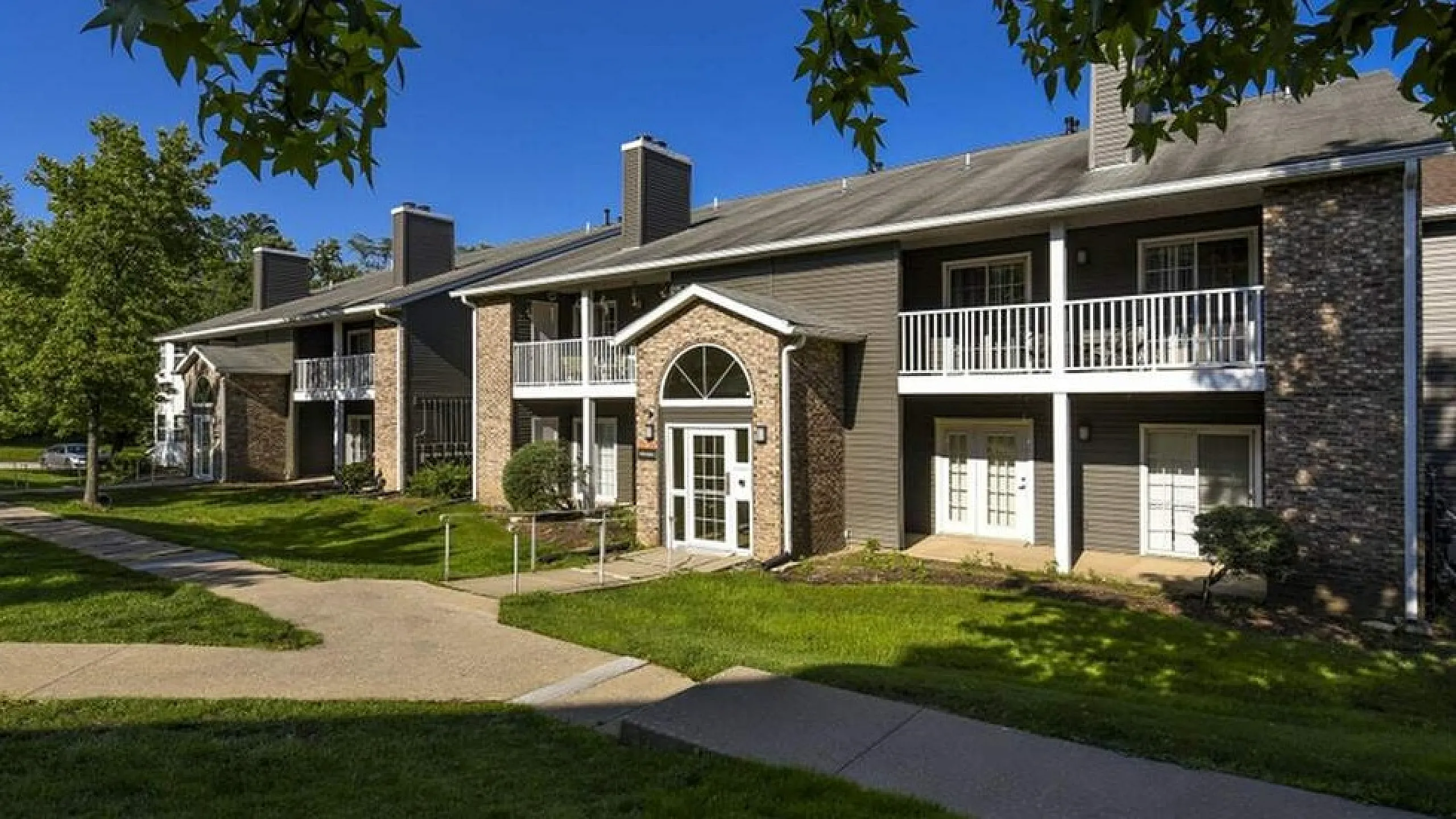 Charming apartment complex with stylish brick facade, elegant balconies, and lush green lawns under a clear blue sky.