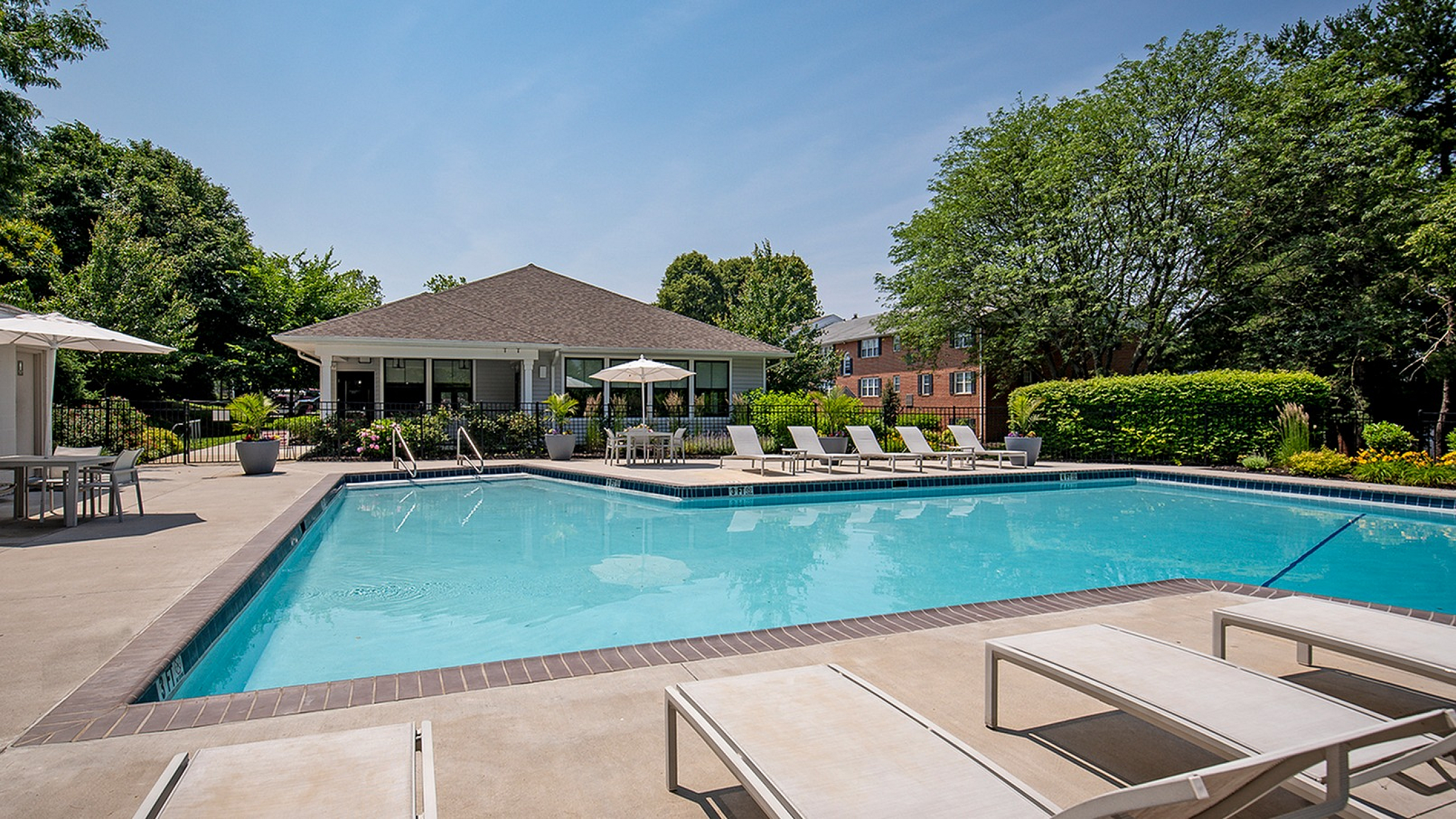 Luxurious outdoor pool area with stylish lounge chairs, surrounded by lush greenery and modern amenities, perfect for relaxation and gatherings.