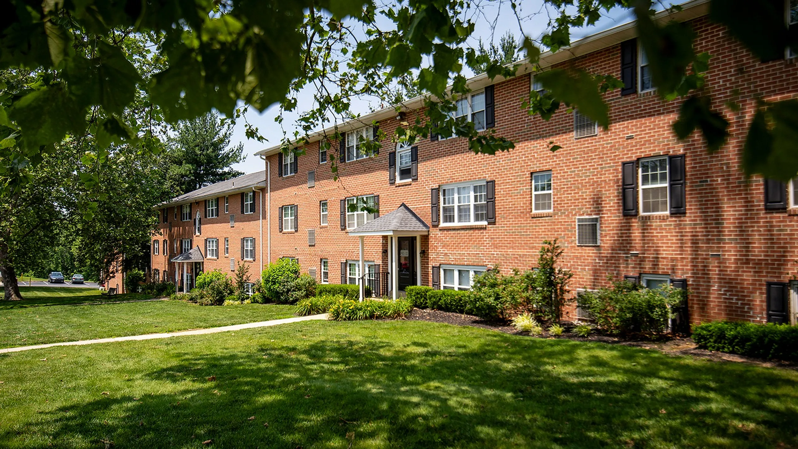 Charming brick apartment building set in lush green surroundings, offering a peaceful residential retreat with beautiful landscaping.