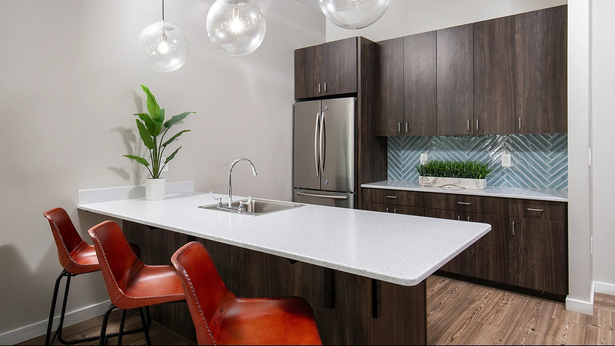 Modern kitchen with sleek design featuring a white quartz island, stylish pendant lighting, and dark wood cabinetry accented by a chic herringbone backsplash.