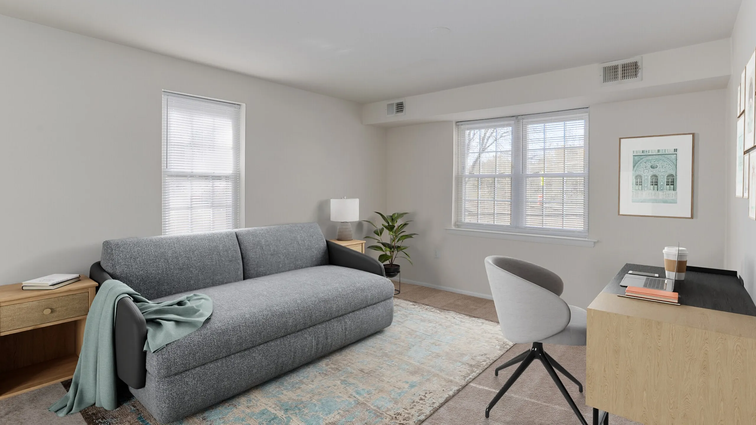 Bright and inviting living space featuring a modern gray sofa, stylish work desk, and large windows for natural light.