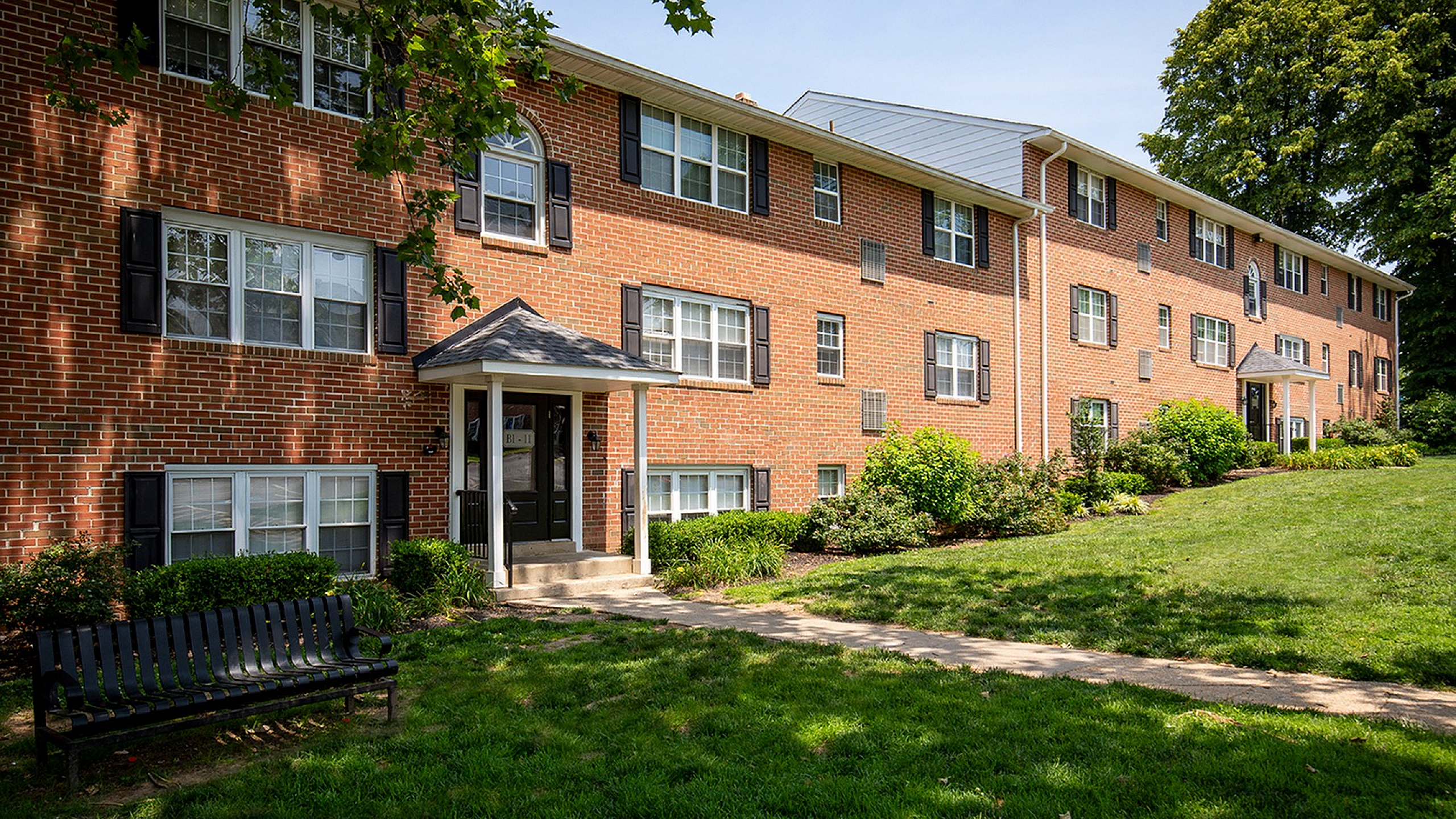 Charming brick apartment building with lush landscaping and inviting entrance, perfect for comfortable suburban living.