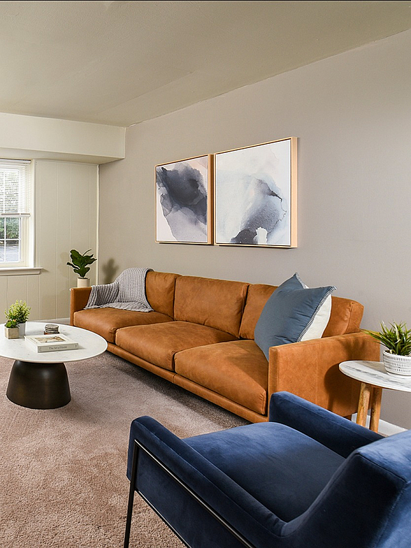 Inviting living room with elegant decor, featuring a spacious orange sofa, stylish armchairs, modern artwork, and lush greenery, offering a warm and welcoming atmosphere.